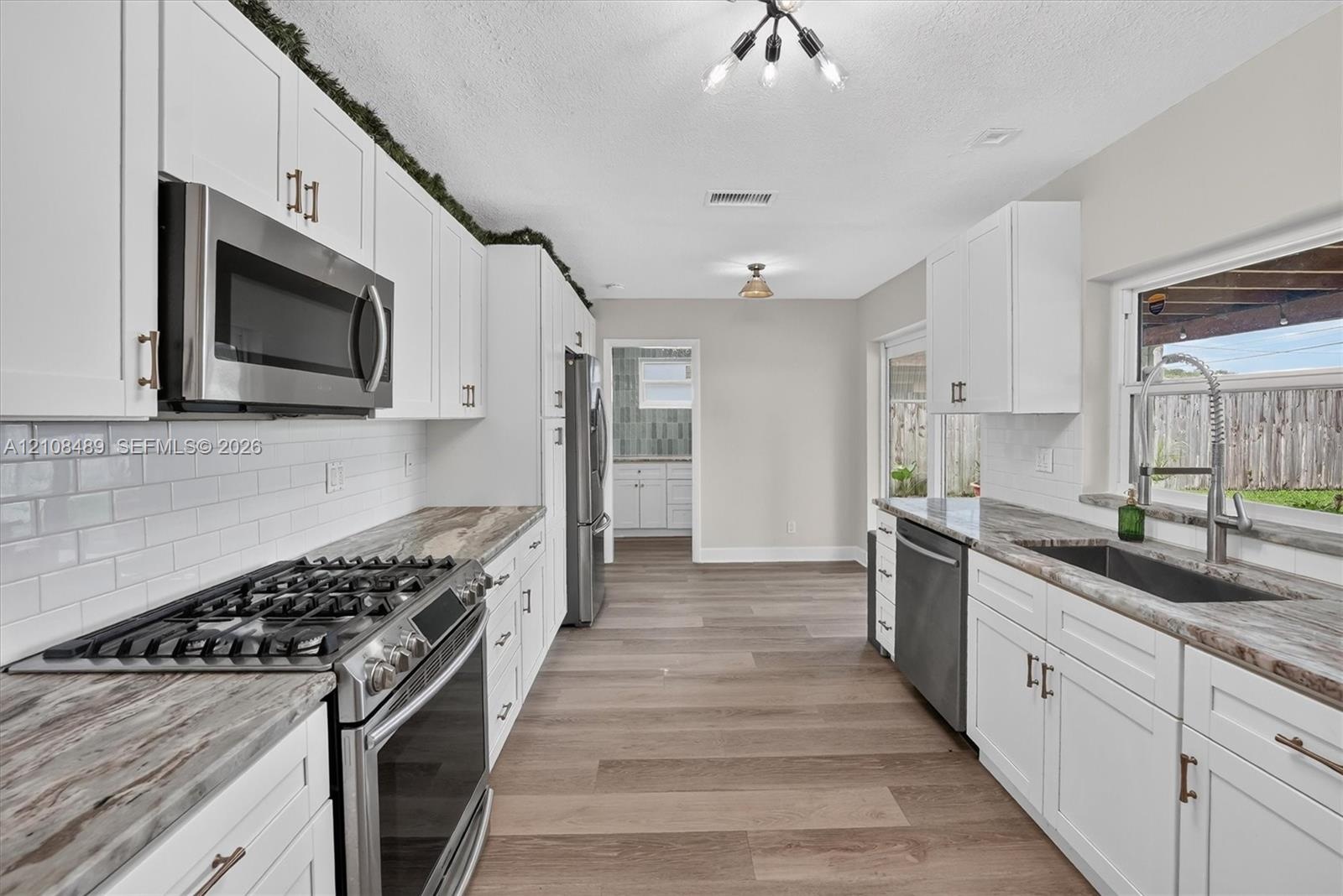 Kitchen featuring white shaker cabinetry, stone-patterned countertops, white subway tile backsplash, stainless steel appliances, and wood-finish floor