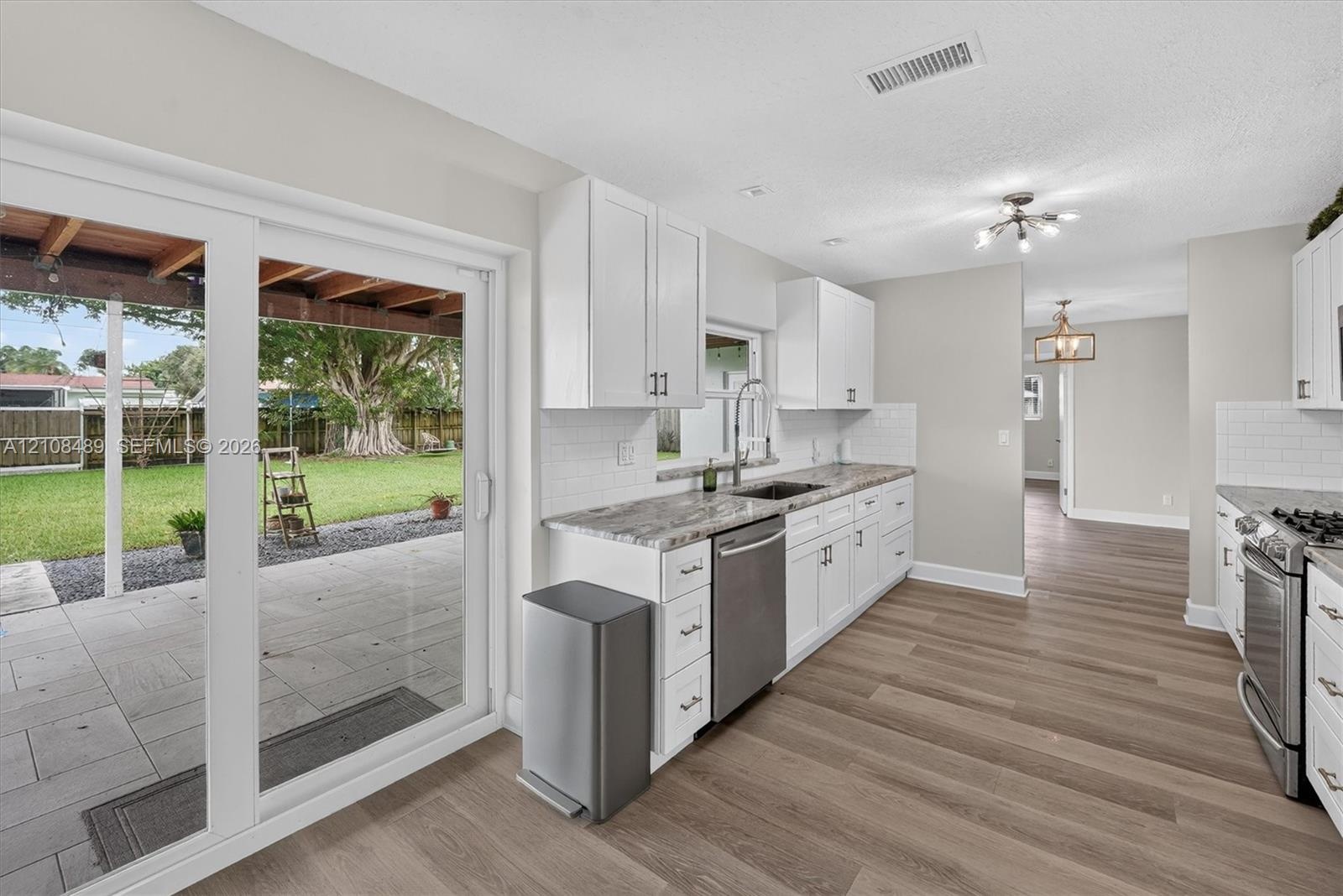 Kitchen featuring white cabinetry, stone-surface countertops, subway tile backsplash, stainless steel appliances, and sliding glass doors to a covered