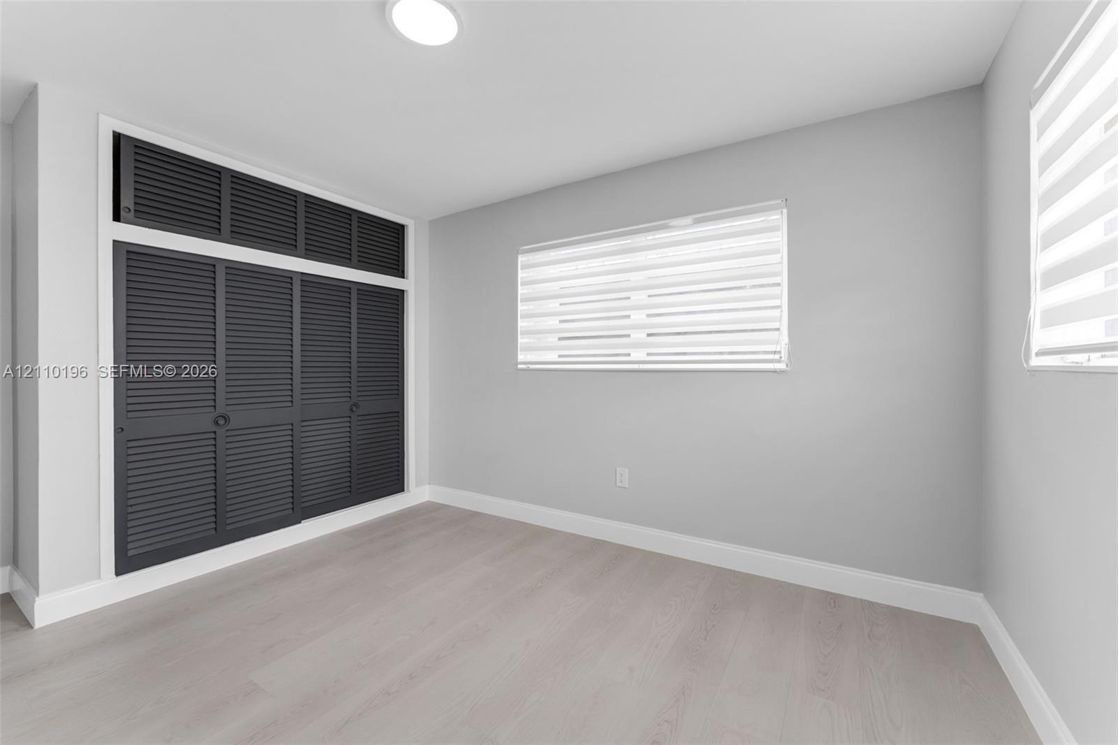 Neutral-toned room featuring wood-finish flooring, built-in floor-to-ceiling louvered-style closet cabinetry with overhead storage, and dual windows w