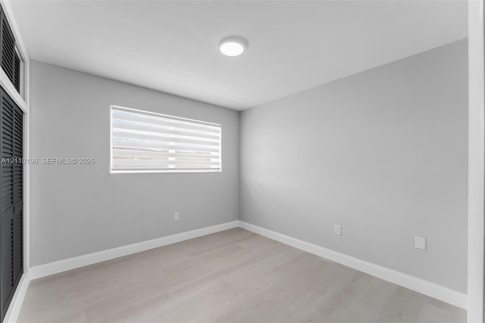 Room featuring wood-finish flooring, neutral wall paint, a flush-mount ceiling light, and louvered-style closet doors