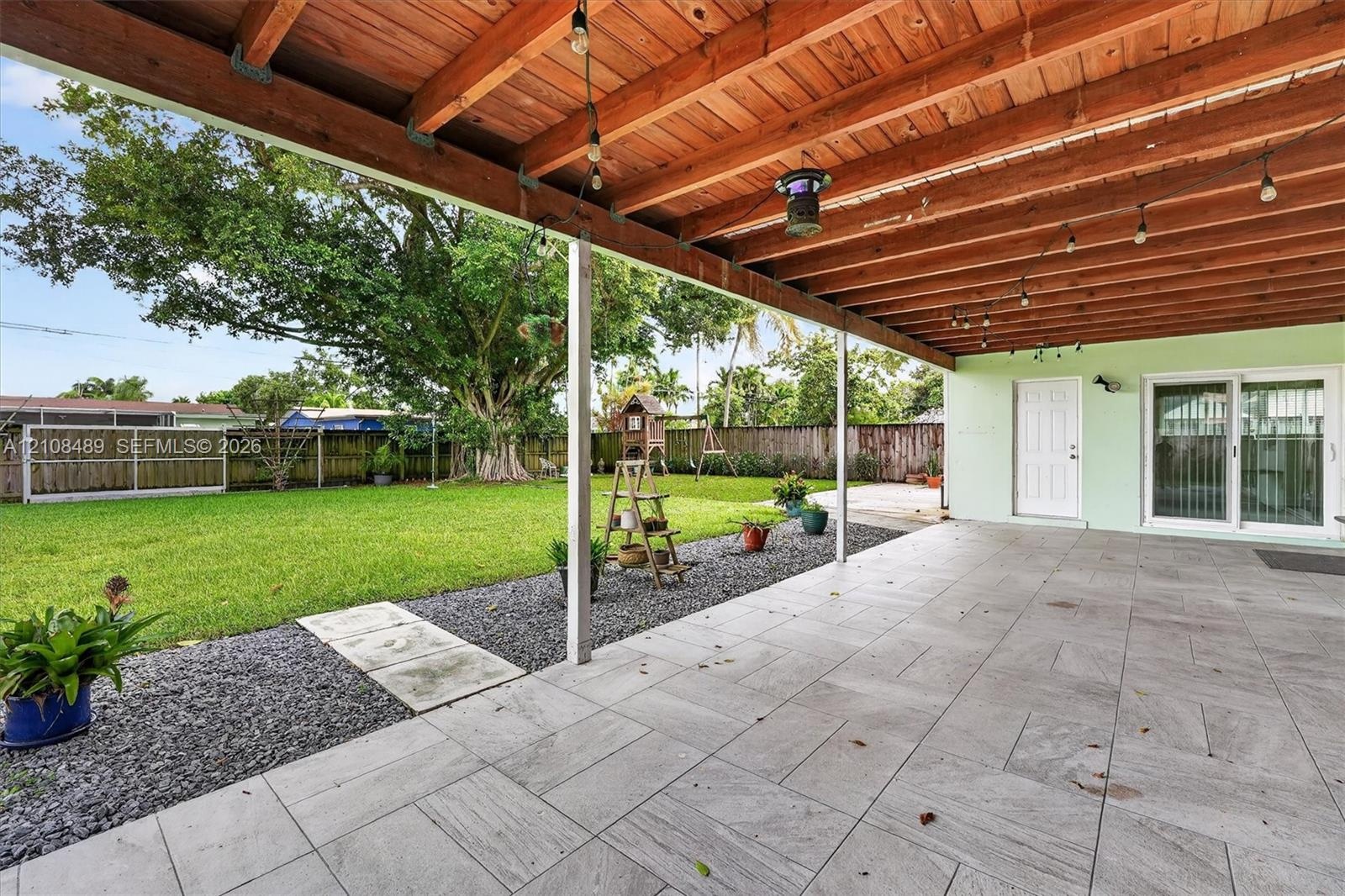Covered patio featuring a wood-beam ceiling, tile flooring, and a large backyard with a privacy fence