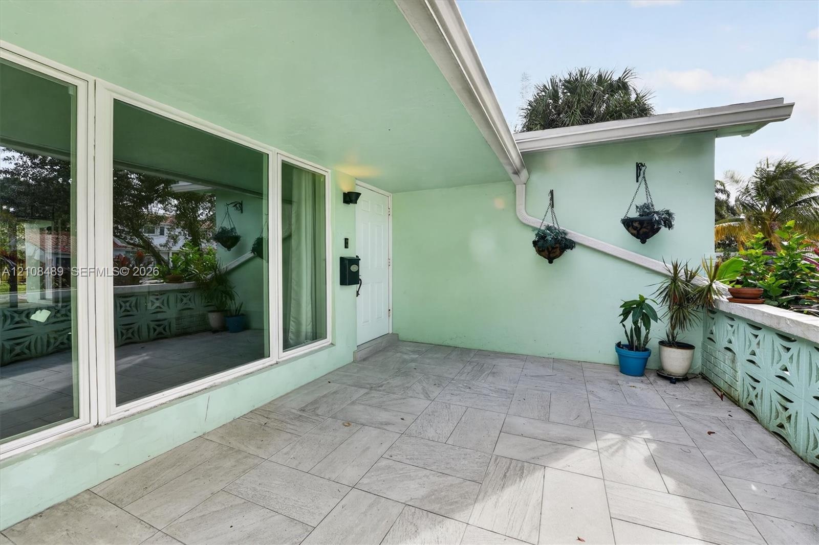 Covered entryway featuring large-format stone-tile flooring, expansive picture windows, and decorative concrete screen block accents