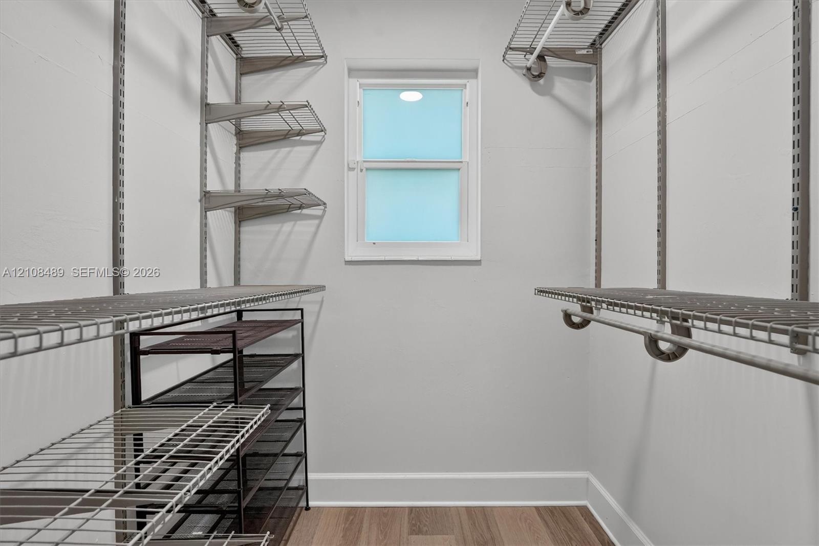 Storage space featuring wall-mounted wire shelving, hanging rods, and wood-finish flooring with a single window