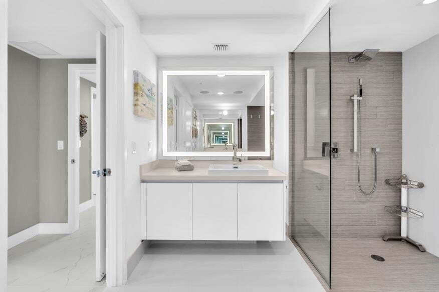Modern bathroom featuring a floating vanity with integrated sink, illuminated mirror, and a glass-enclosed shower with a rain showerhead