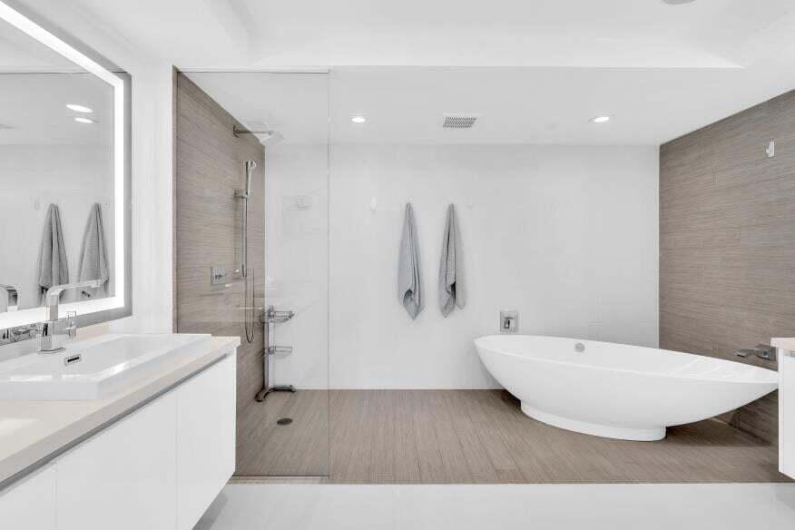 Modern bathroom with a freestanding soaking tub, glass-enclosed shower, wood-finish flooring, and a vanity with an illuminated mirror