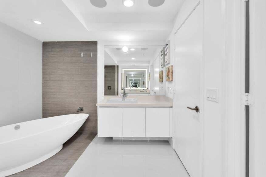 Freestanding soaking tub with a tiled accent wall, single vanity with integrated sink, and large mirror with integrated lighting