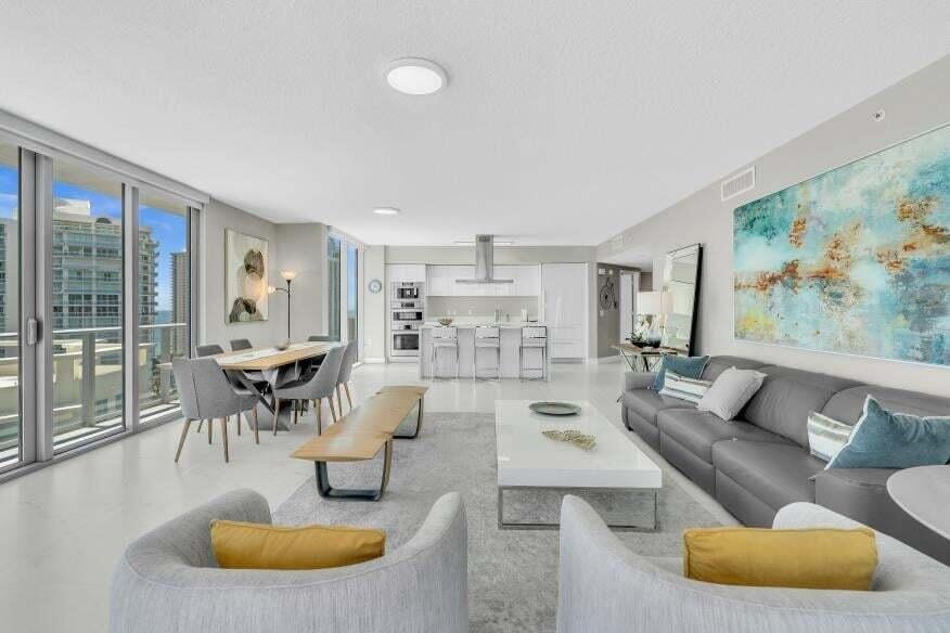 Open-concept living space with expansive sliding glass doors, white flooring, recessed lighting, and a modern kitchen with built-in appliances