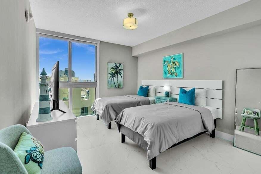 Expansive window with city background, overhead ceiling light fixture, white headboards, and light-toned flooring