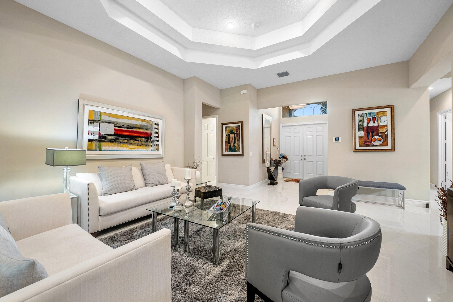 Living area featuring a multi-tiered tray ceiling, polished tile flooring, recessed lighting, and double-entry doors with a transom window