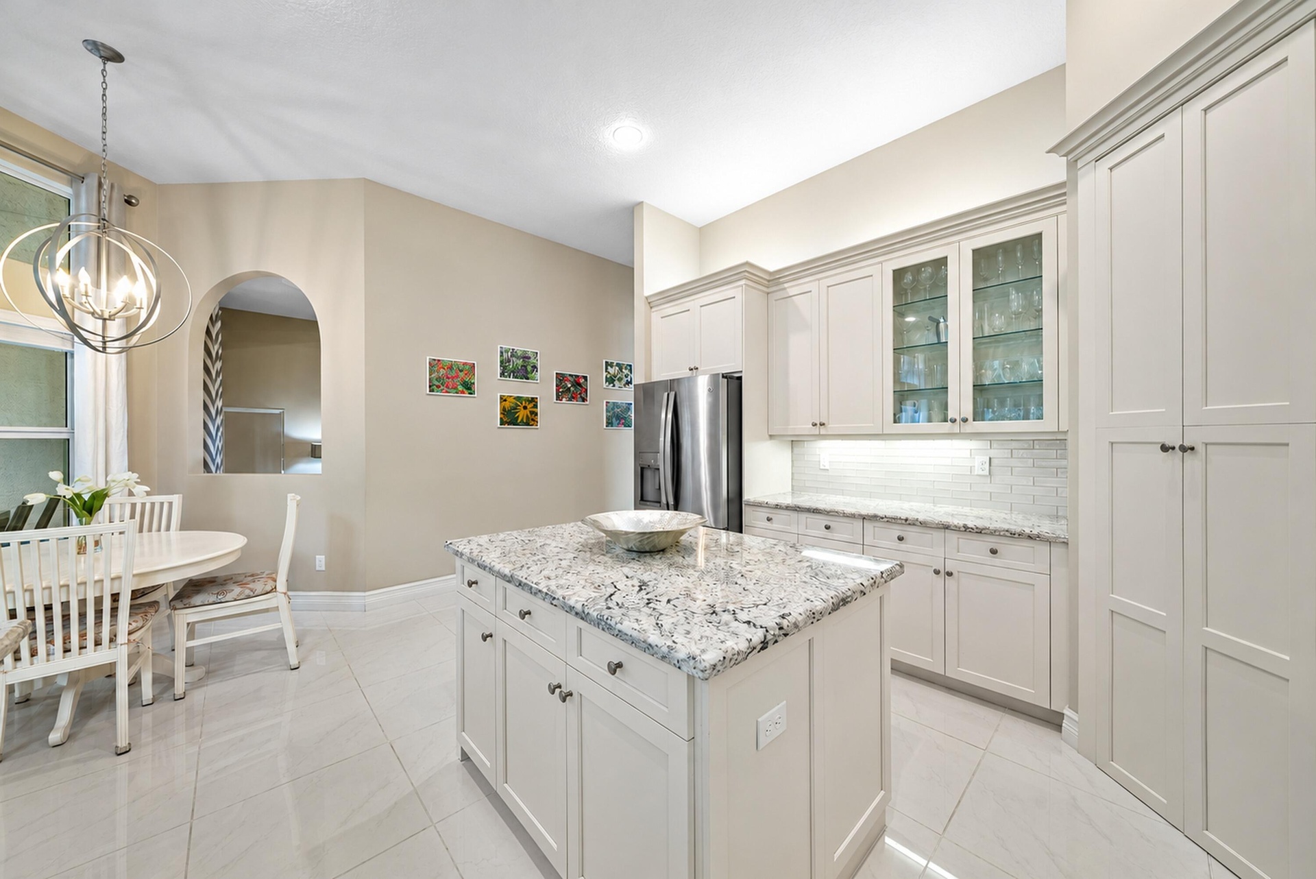 Kitchen featuring custom cabinetry with glass-front display uppers, a central island with stone countertop, stainless steel refrigerator, and tiled fl