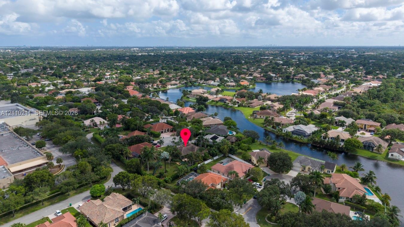 Aerial perspective of a residential property situated in a suburban community, featuring mature tropical landscaping and proximity to a winding waterw
