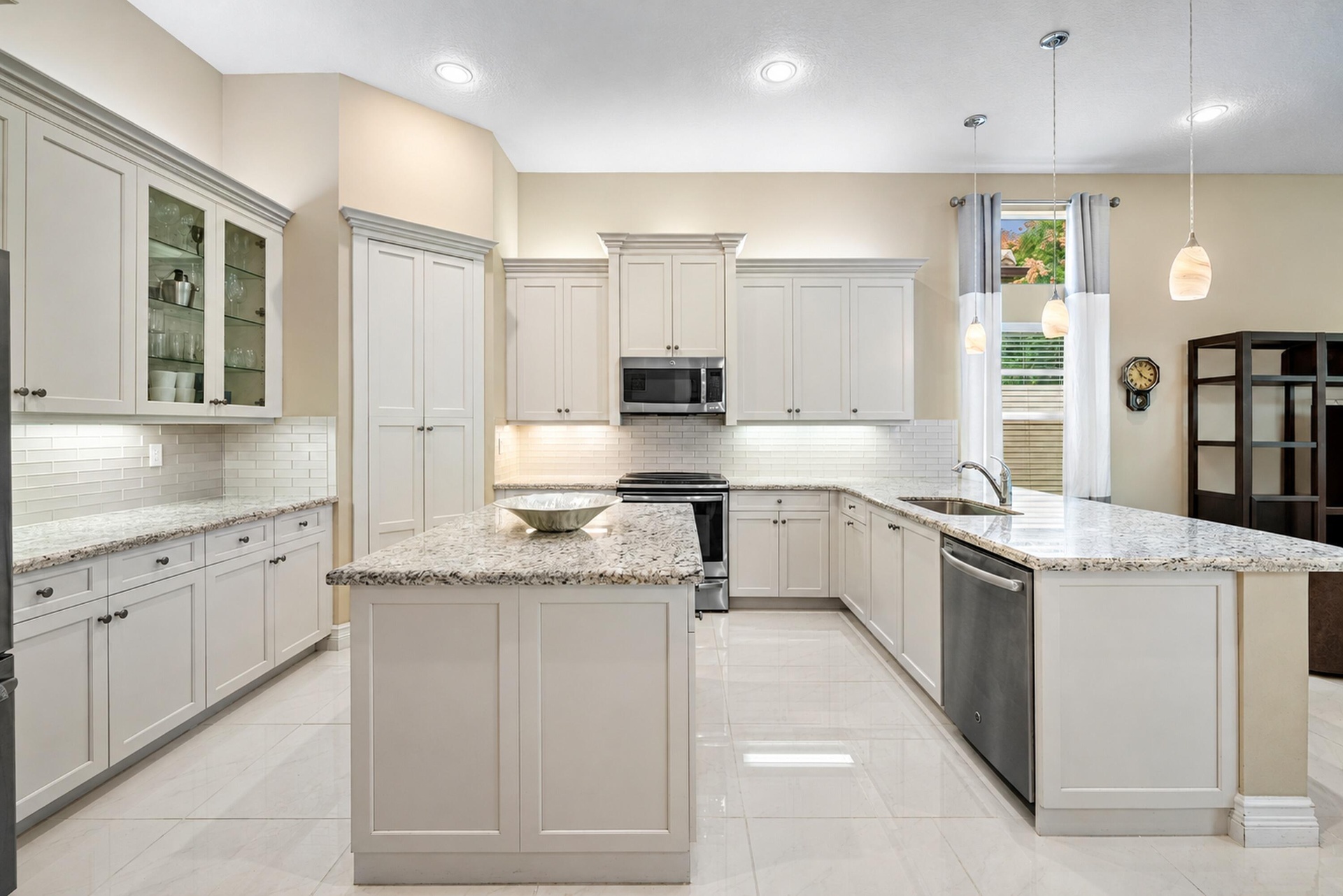 Kitchen featuring light-toned cabinetry, stone-surface countertops, central island, tiled backsplash, and stainless-steel appliances
