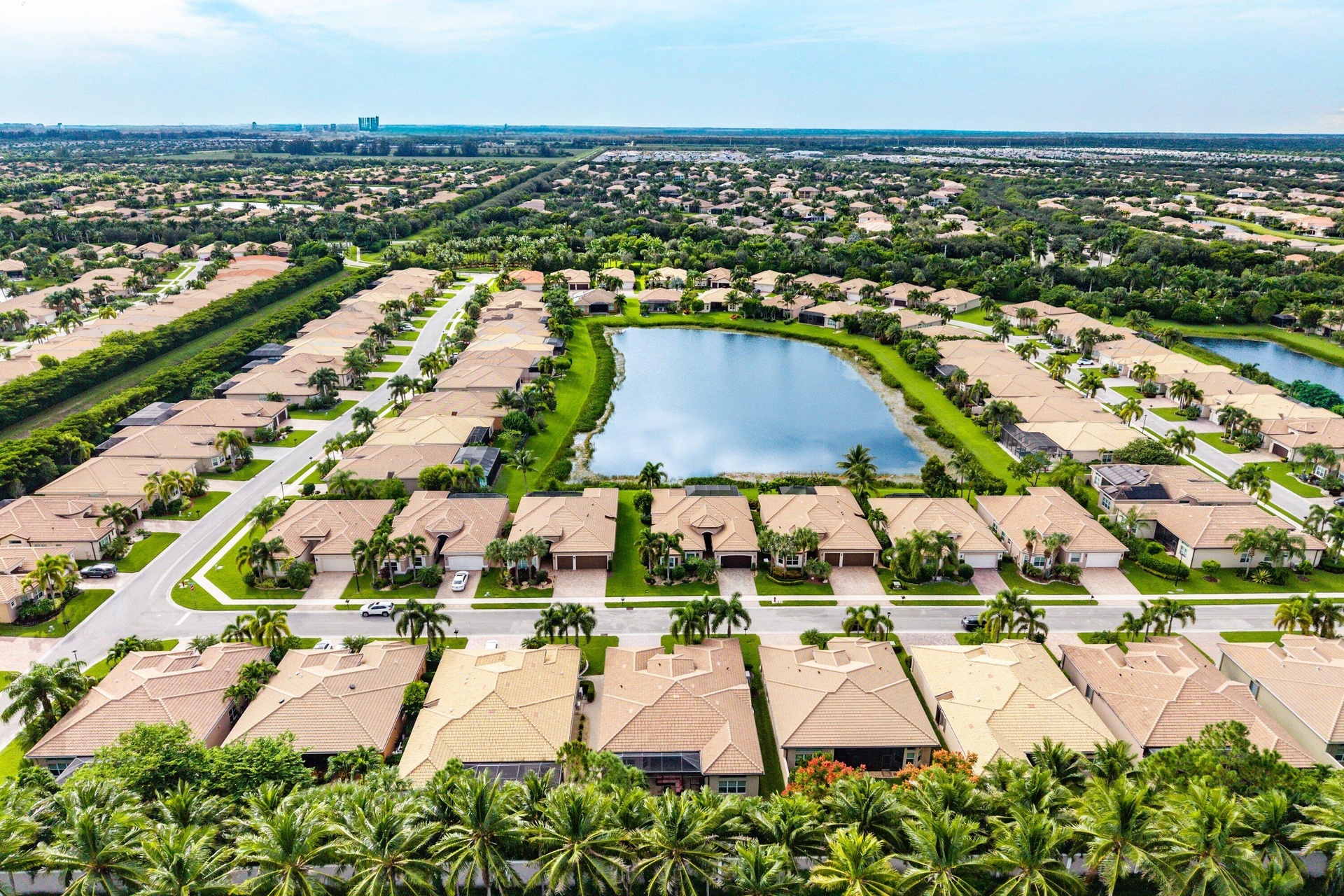 Aerial perspective of a residential community centered around a large lake, featuring multiple tile-roof homes, paved street infrastructure, and estab