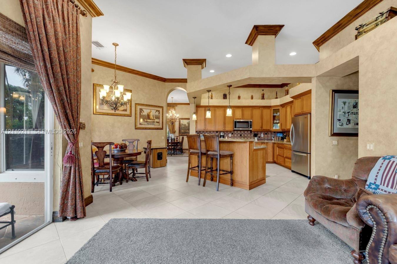 Open-concept kitchen featuring wood cabinetry, stainless steel appliances, a breakfast bar, recessed lighting, and tile flooring