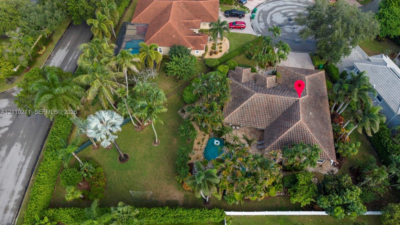 Aerial perspective of a property featuring a tile roof, an in-ground swimming pool, extensive landscaping with mature palm trees, and a perimeter fenc