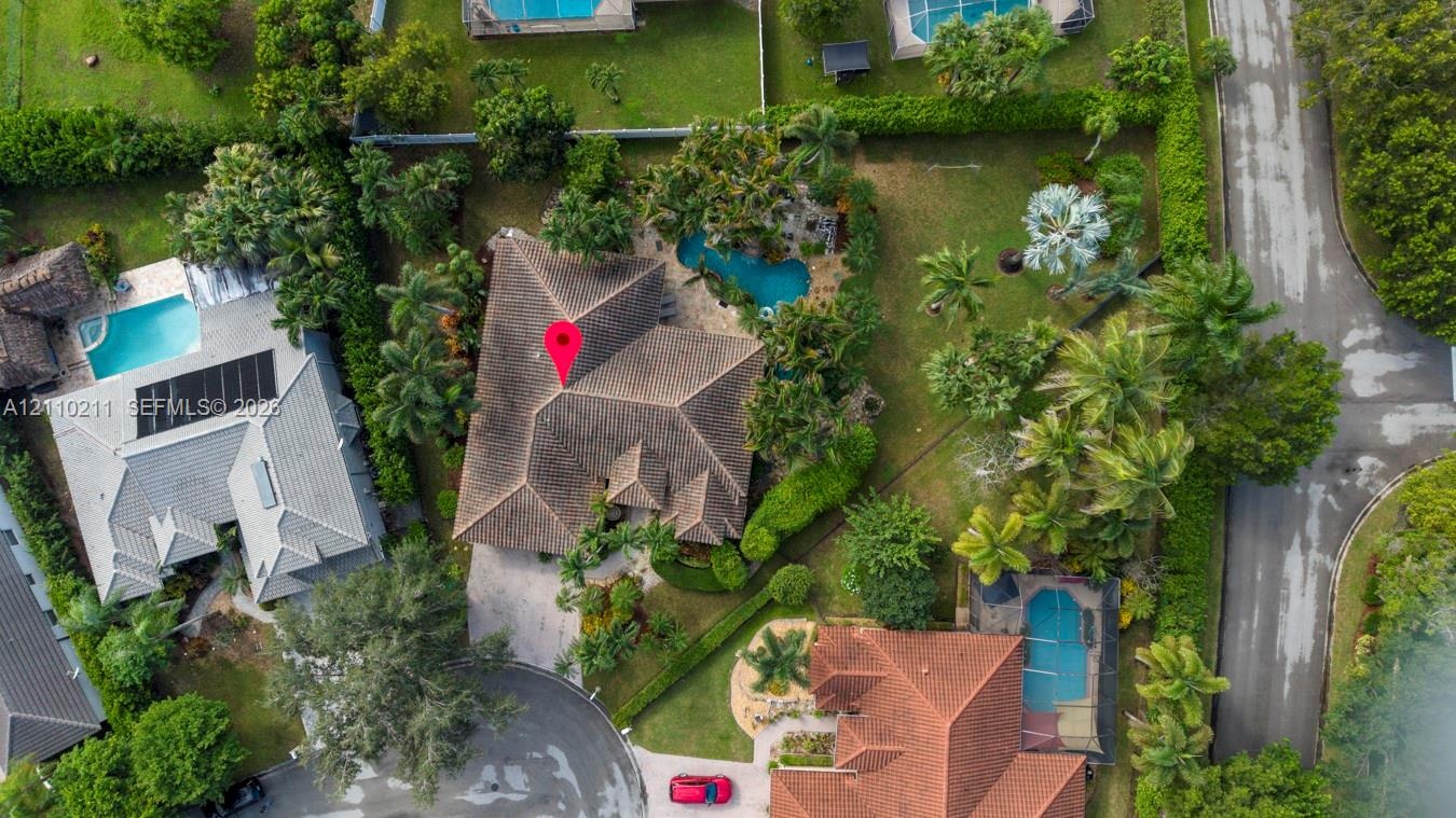 Aerial view featuring a multi-hipped roofline, an in-ground swimming pool, mature palm trees, and landscaped grounds