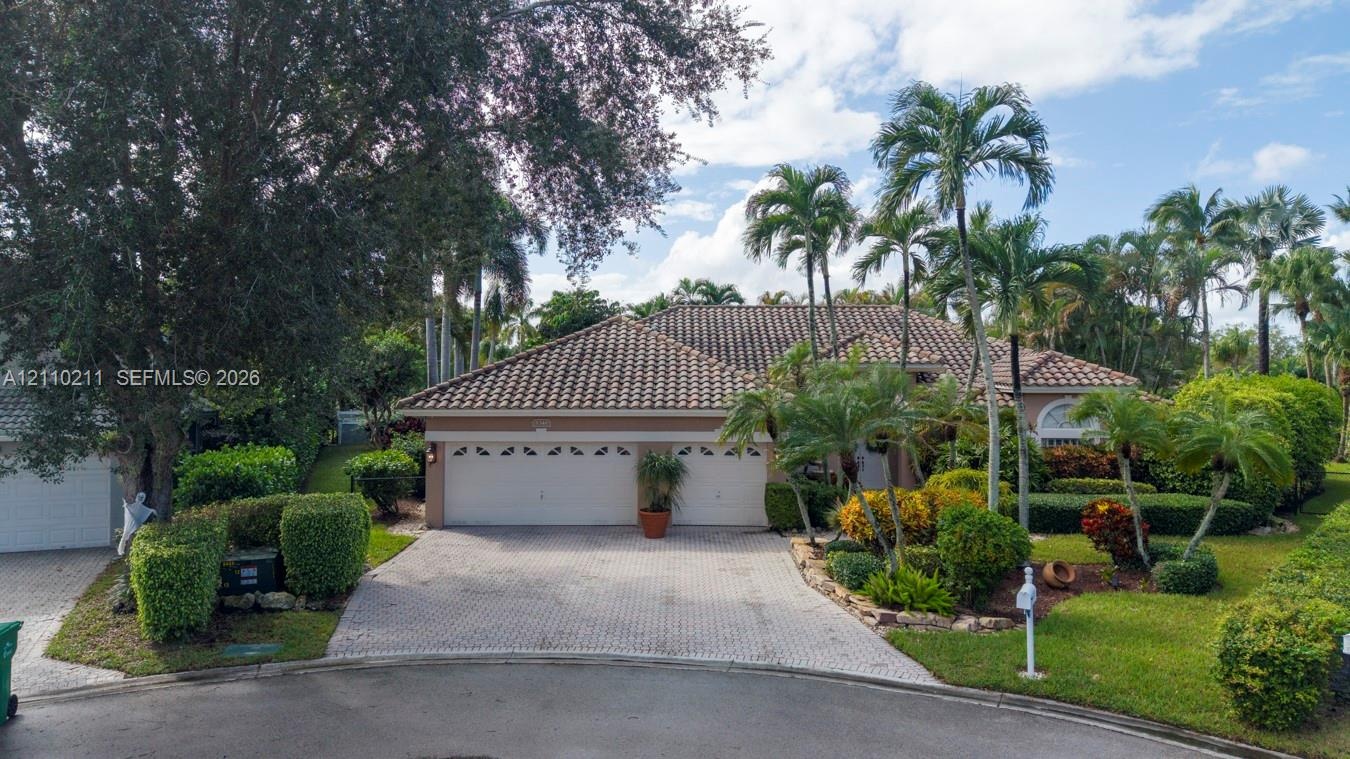 Exterior featuring a tile roof, two-car garage, paver driveway, and mature tropical landscaping