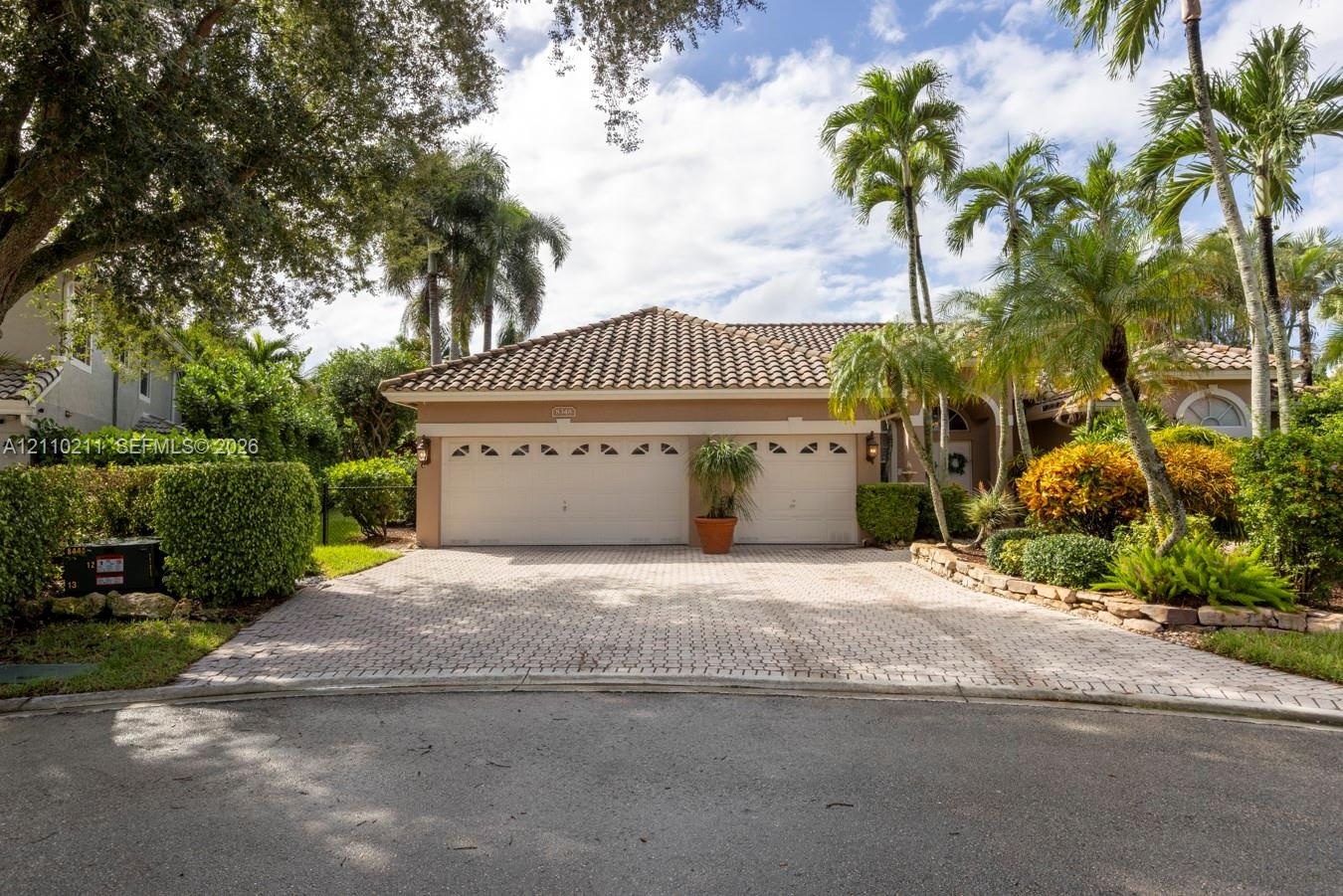 Exterior featuring a two-car garage, tiled roof, paved driveway, and mature landscaping