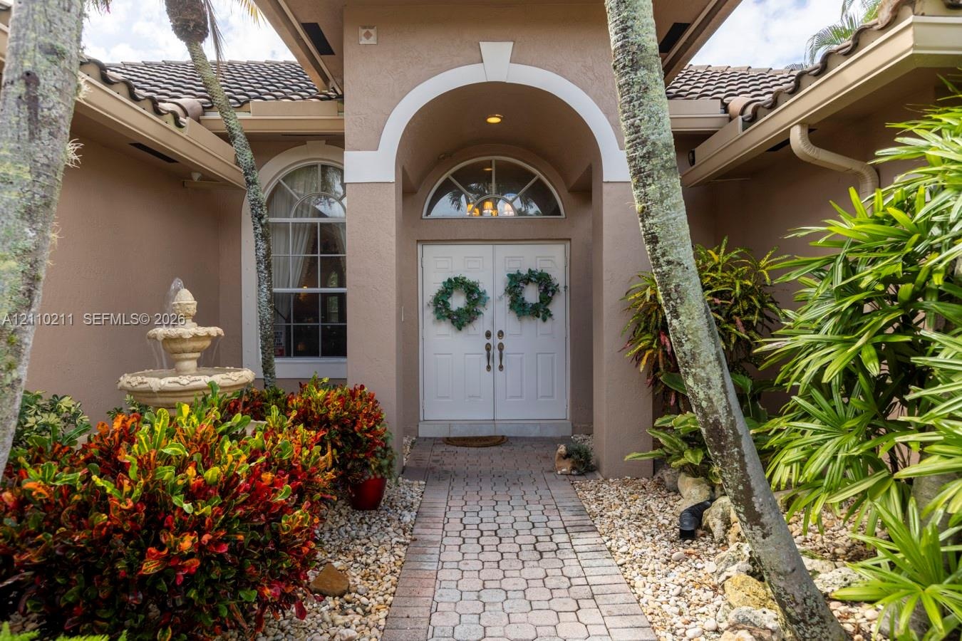Covered entryway featuring a stone-paver walkway, arched portico, double-door entry with a semi-circular transom window, and an integrated stone fount