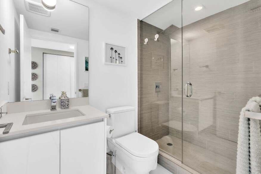 Modern bathroom featuring a frameless glass shower enclosure, a full-height vanity mirror, a single-sink vanity with white cabinetry, and a walk-in sh