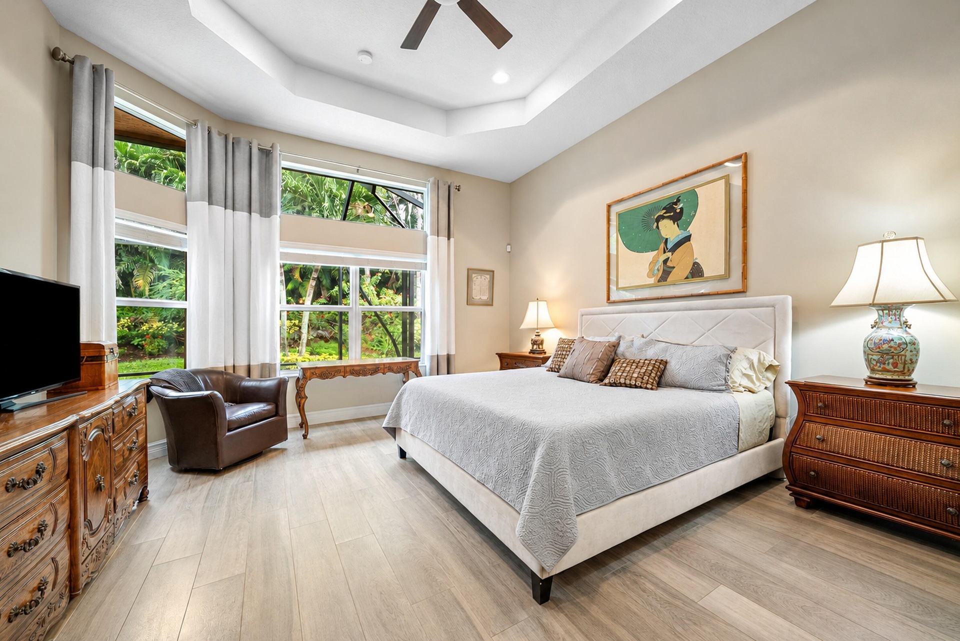 Tray ceiling with a central fan, light-toned wood-finish flooring, and multiple tiers of windows