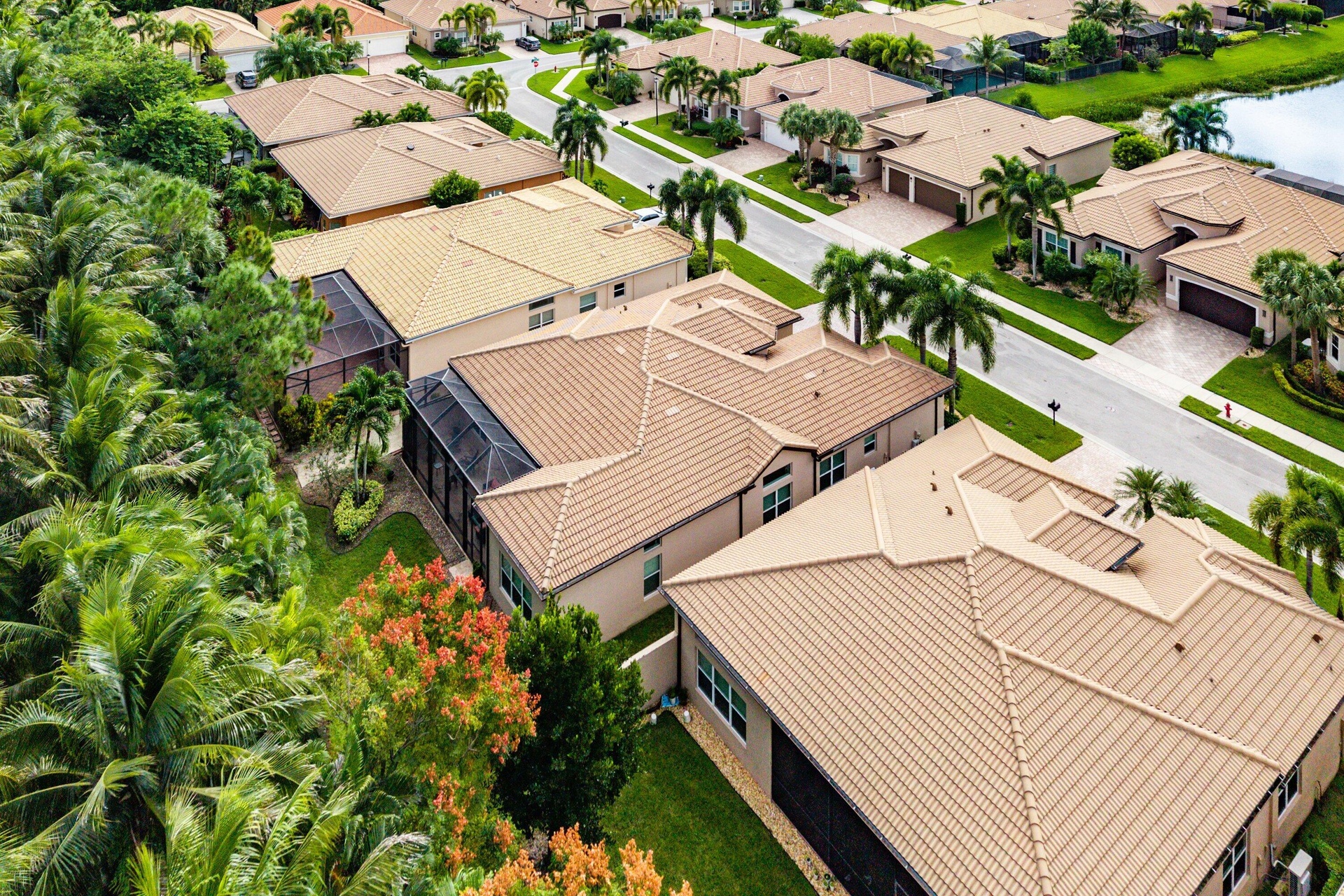 Aerial view of a residential property featuring a tiled roof, screened-in rear patio, two-car garage, and established landscaping
