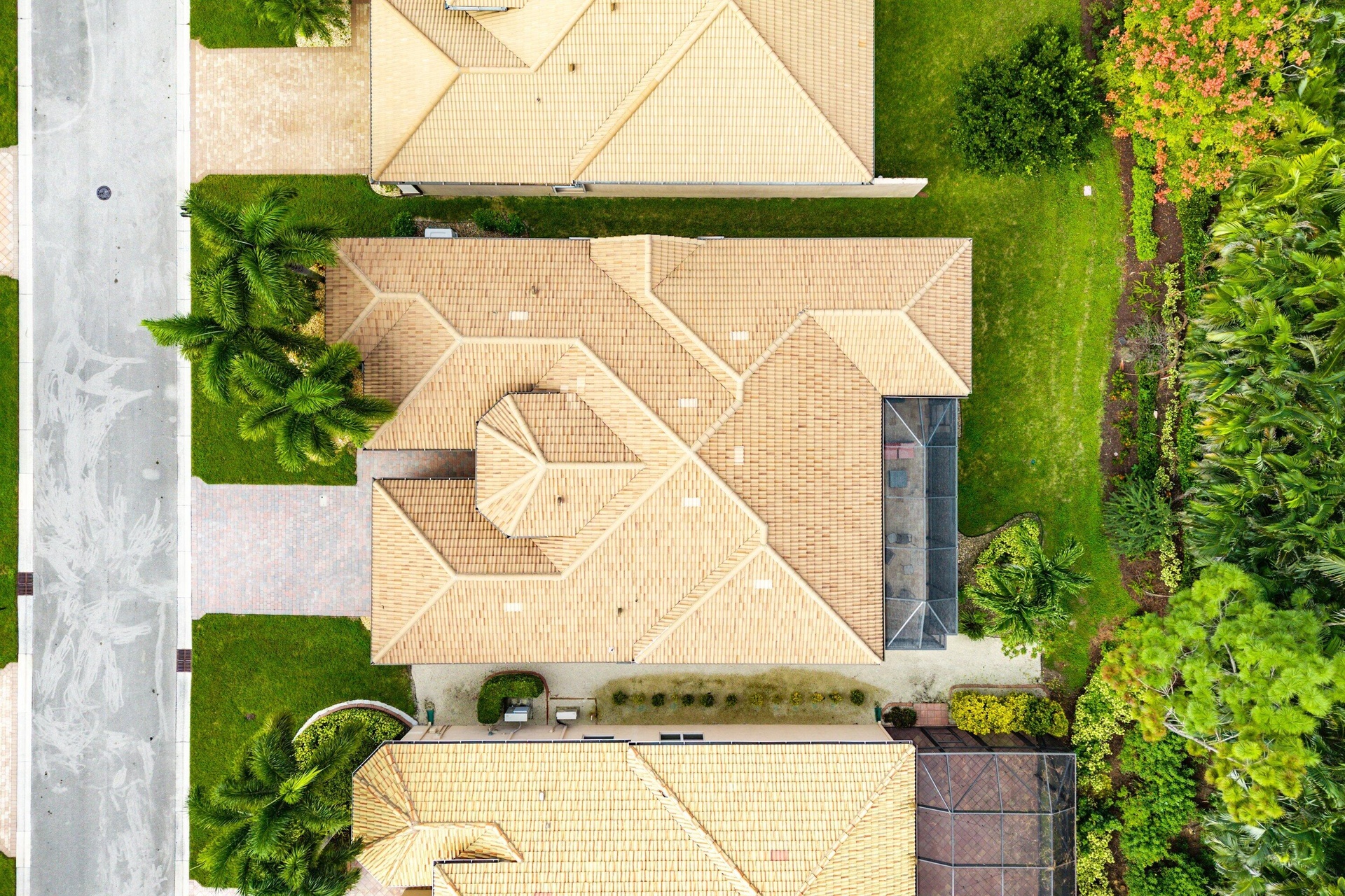 Aerial view featuring a multi-gabled tile roof, a screened-in enclosure, concrete driveway, and landscaped perimeter