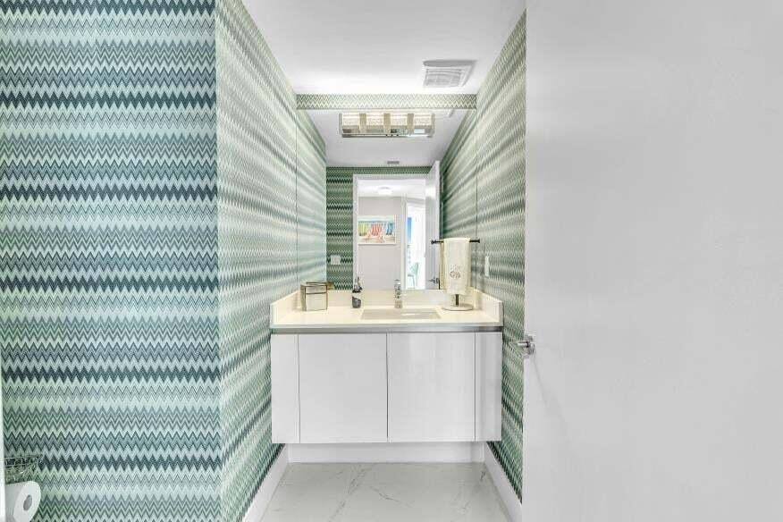 Floating vanity with a light-toned countertop, under-mount sink, and chevron-patterned wall covering