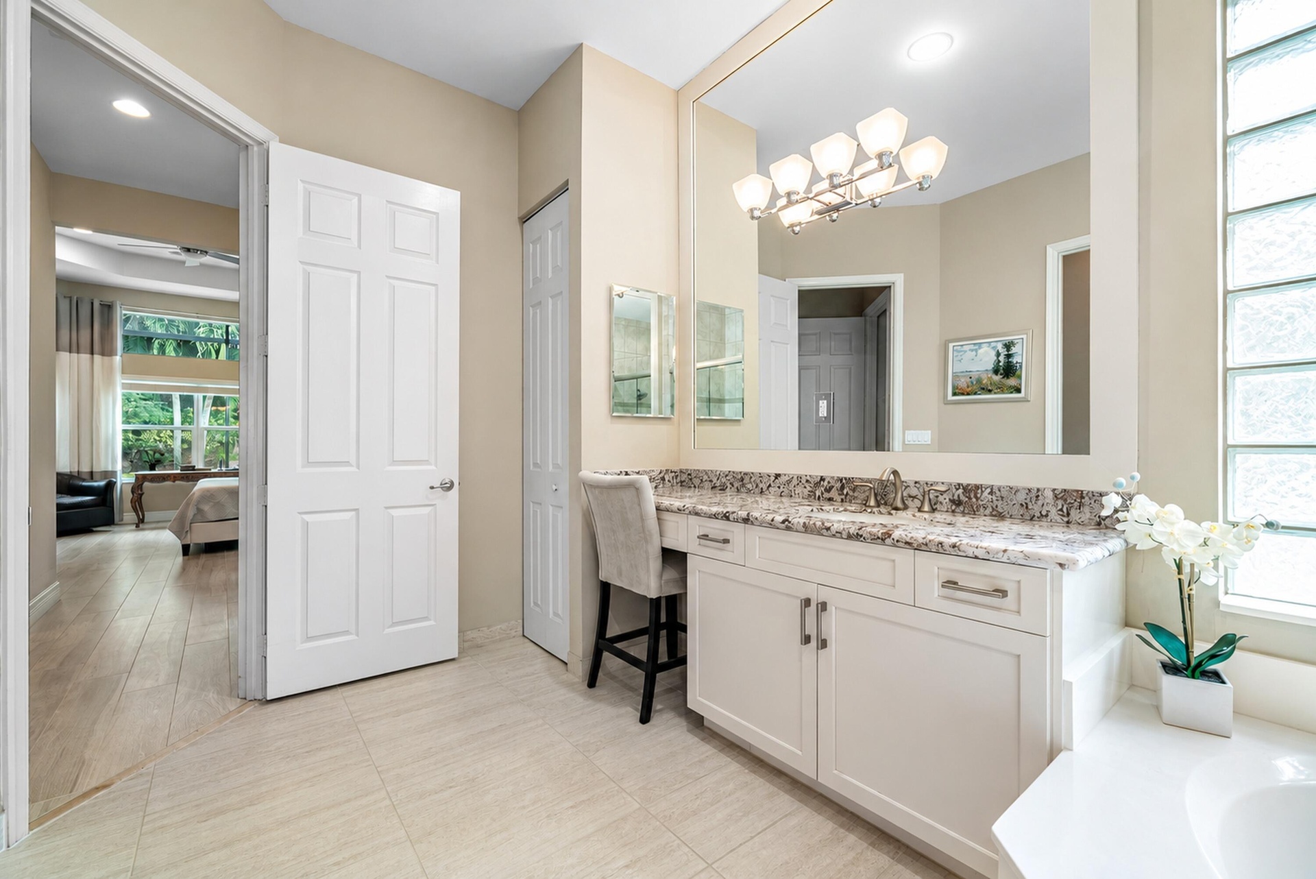 Bathroom vanity featuring white cabinetry, stone-surface countertop with an integrated sink, full-width wall mirror, multi-bulb light fixture, and tra