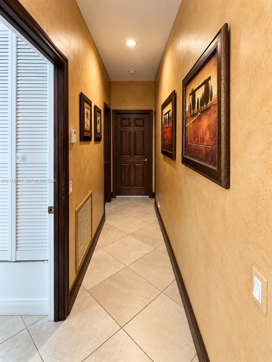 Hallway featuring neutral-toned textured wall finishes, tile flooring laid on a diagonal, recessed ceiling lighting, and solid wood-finish doors with 