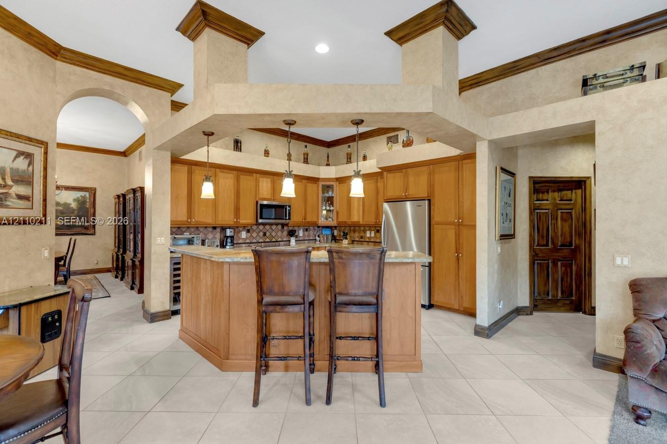 Kitchen featuring custom wood cabinetry, stone countertops, a multi-tiered peninsula island, tile flooring, and hanging pendant lighting