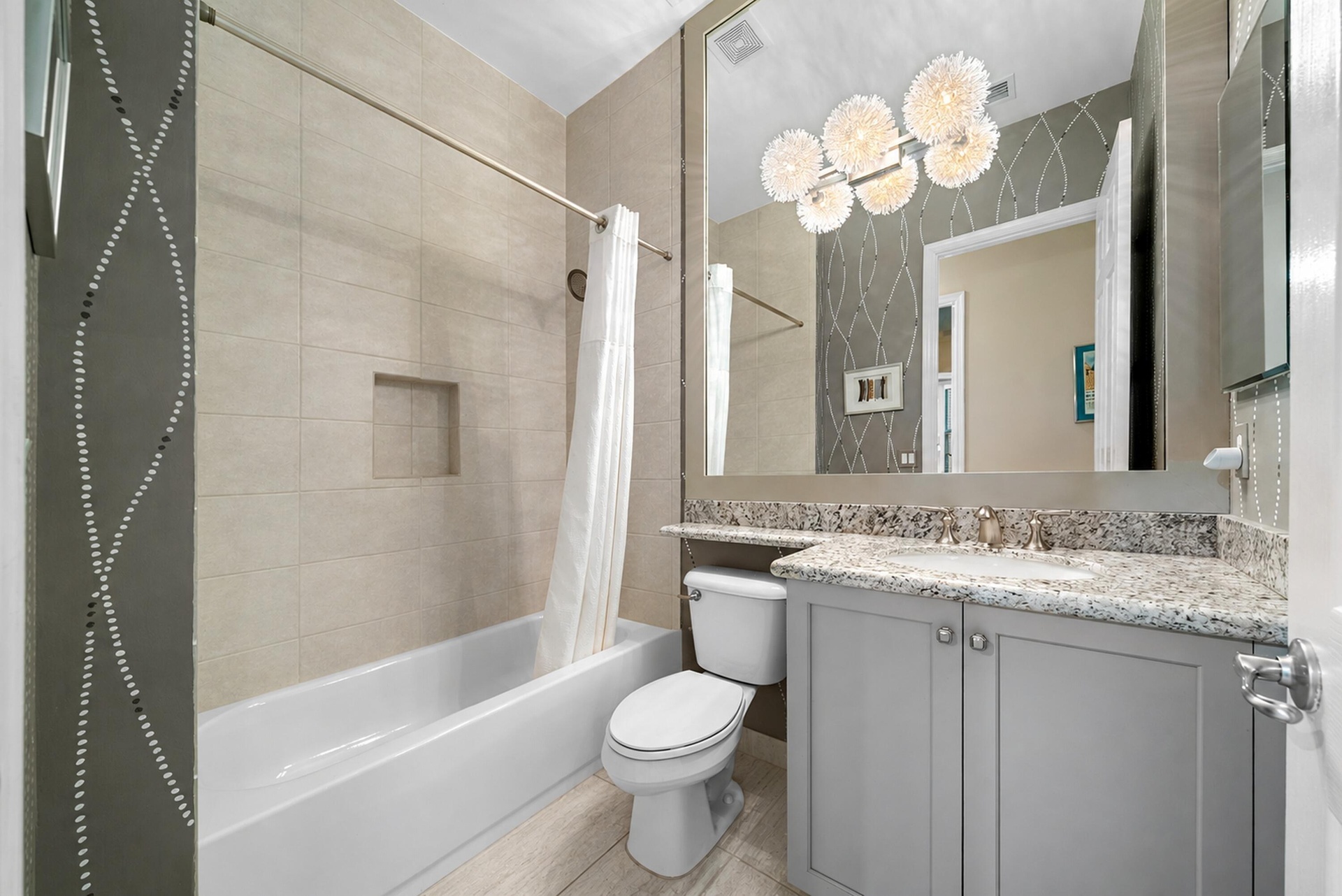 Bathroom featuring a vanity with stone countertop, integrated sink, large wall-mounted mirror, multi-light fixture, and tub with tiled surround and in