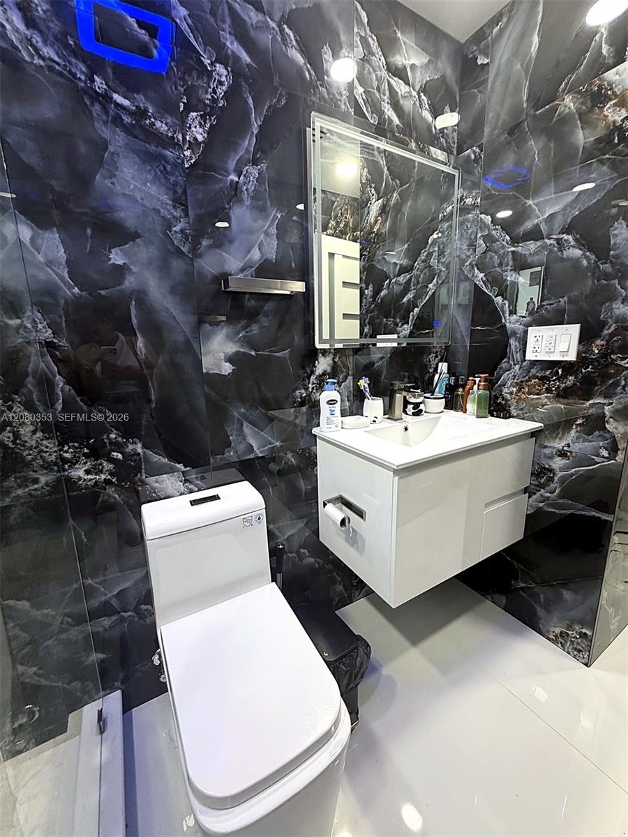 Floor-to-ceiling high-contrast decorative wall tile, white floating vanity, integrated rectangular basin, contemporary low-profile toilet, and rectang