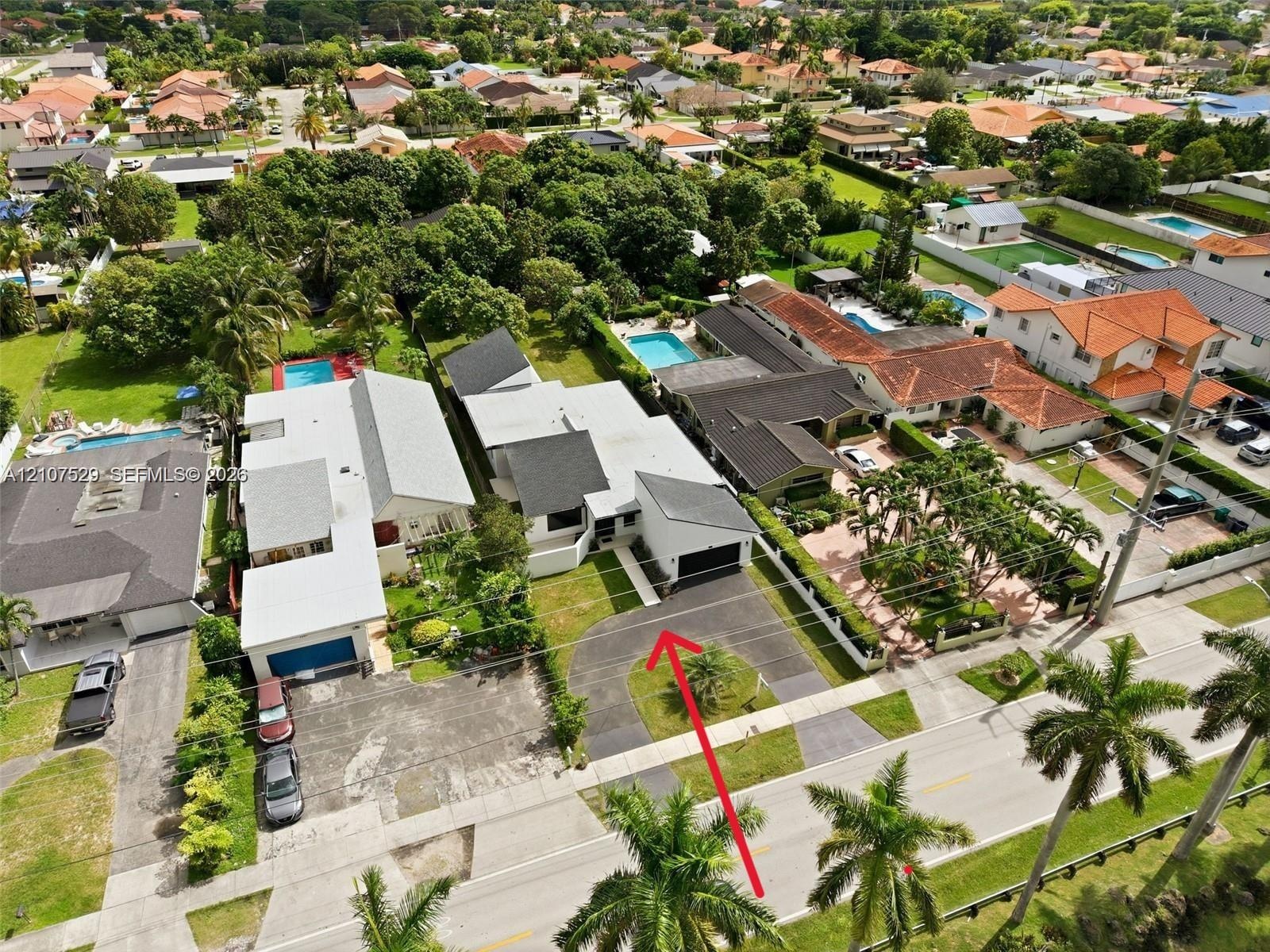 Aerial perspective of a single-story residence featuring a shingled roof, an attached garage, a paved driveway, and established landscaping