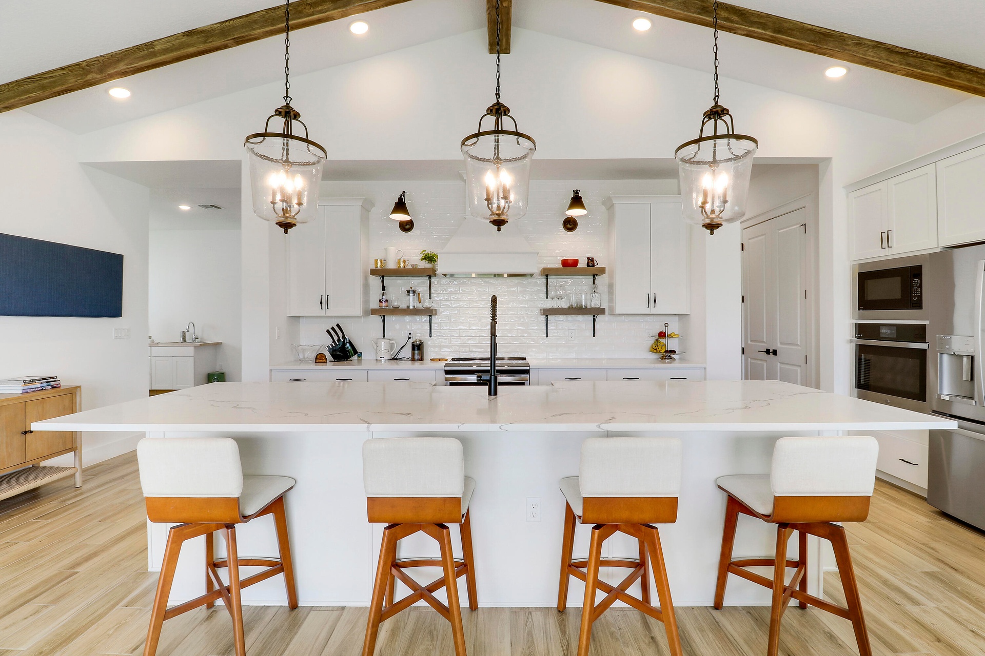 Kitchen featuring a central island with a stone-finish countertop, vaulted ceiling with exposed wood-finish like beams, white cabinetry, lantern-style