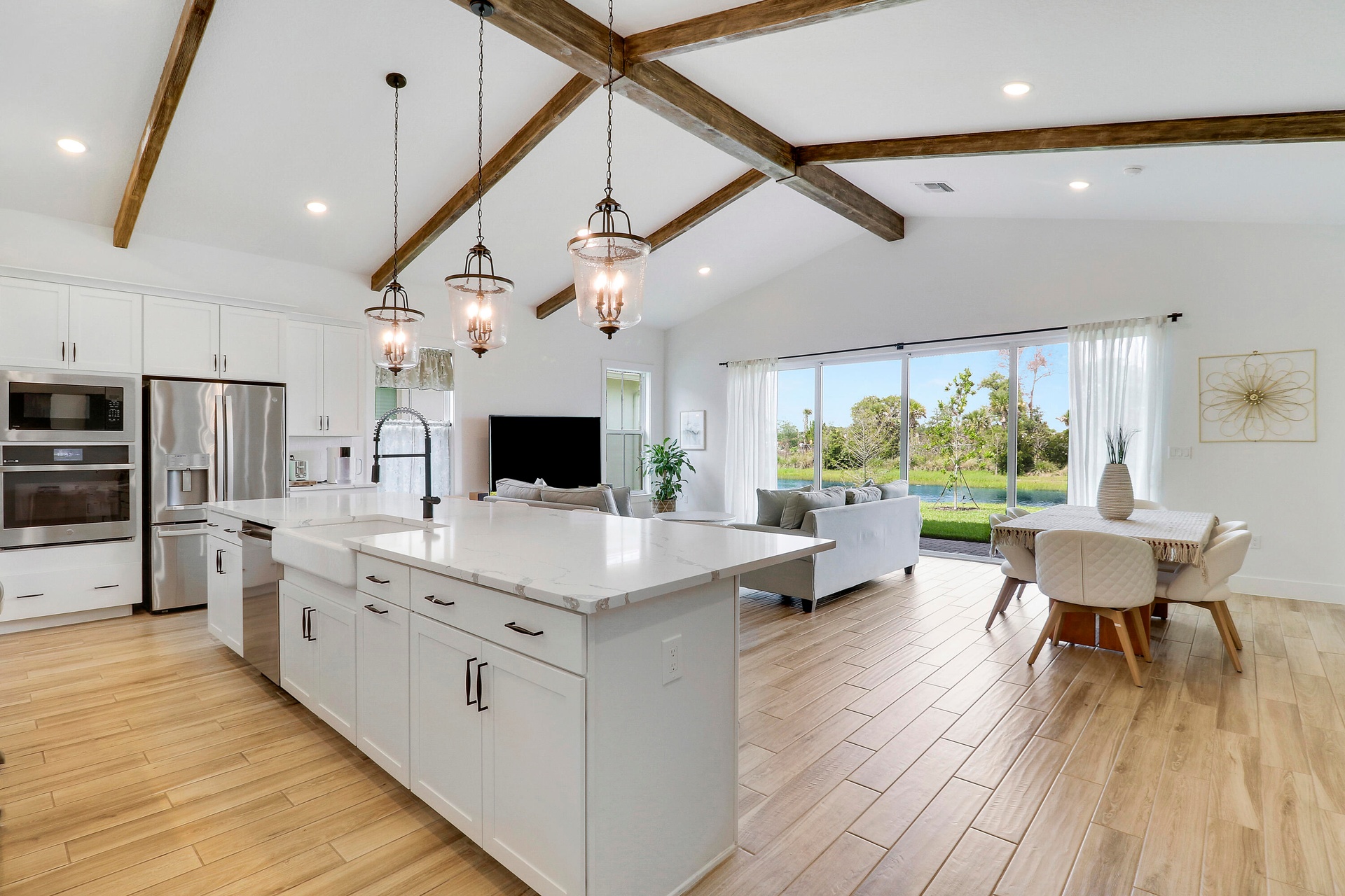 Kitchen featuring vaulted ceilings imitating wood beams, an expansive center island with a farmhouse-style sink, quartz countertops, pendant lighting,