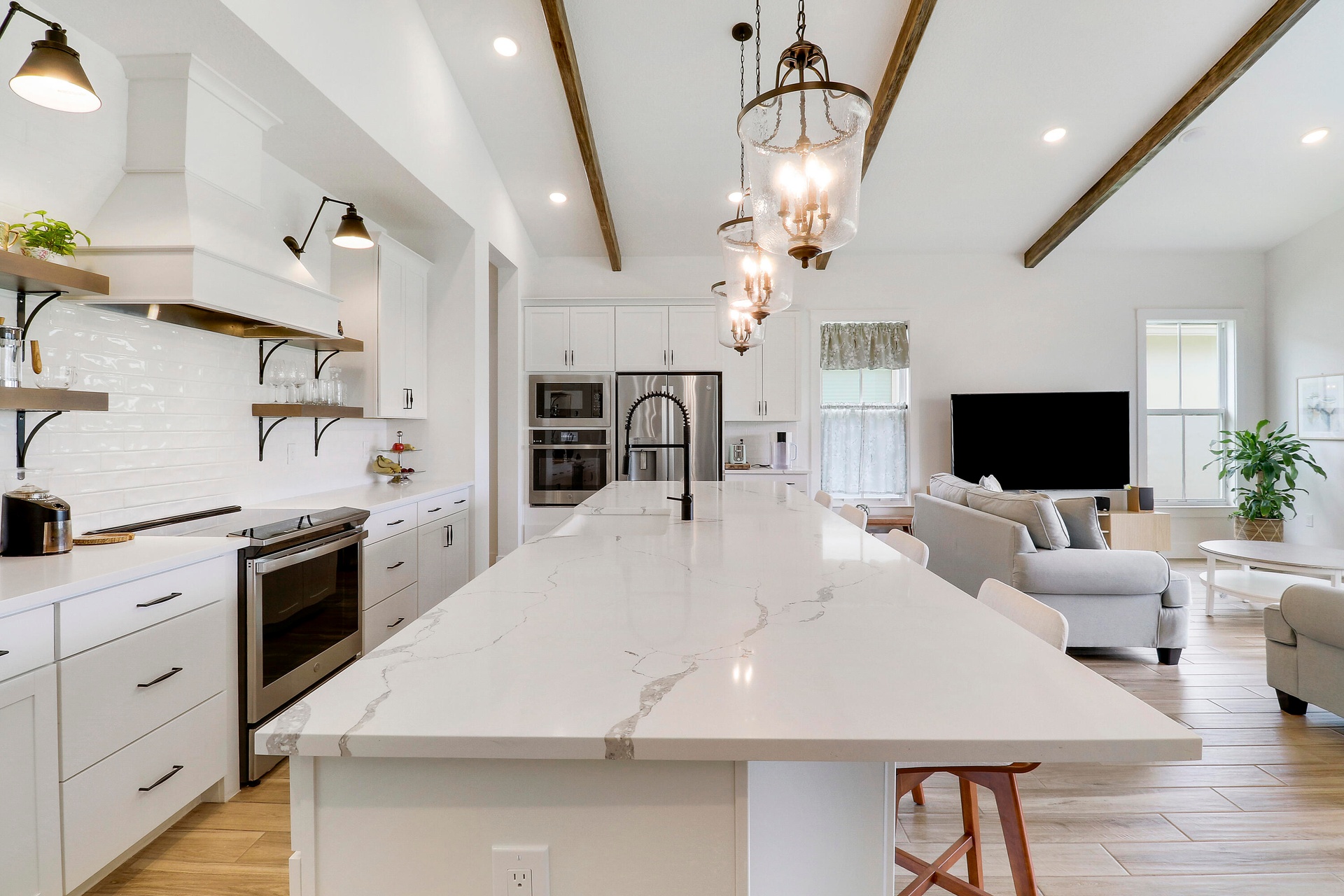 Kitchen featuring a central island with a stone countertop, white shaker cabinetry, stainless steel built-in appliances, decorative ceiling beams, and