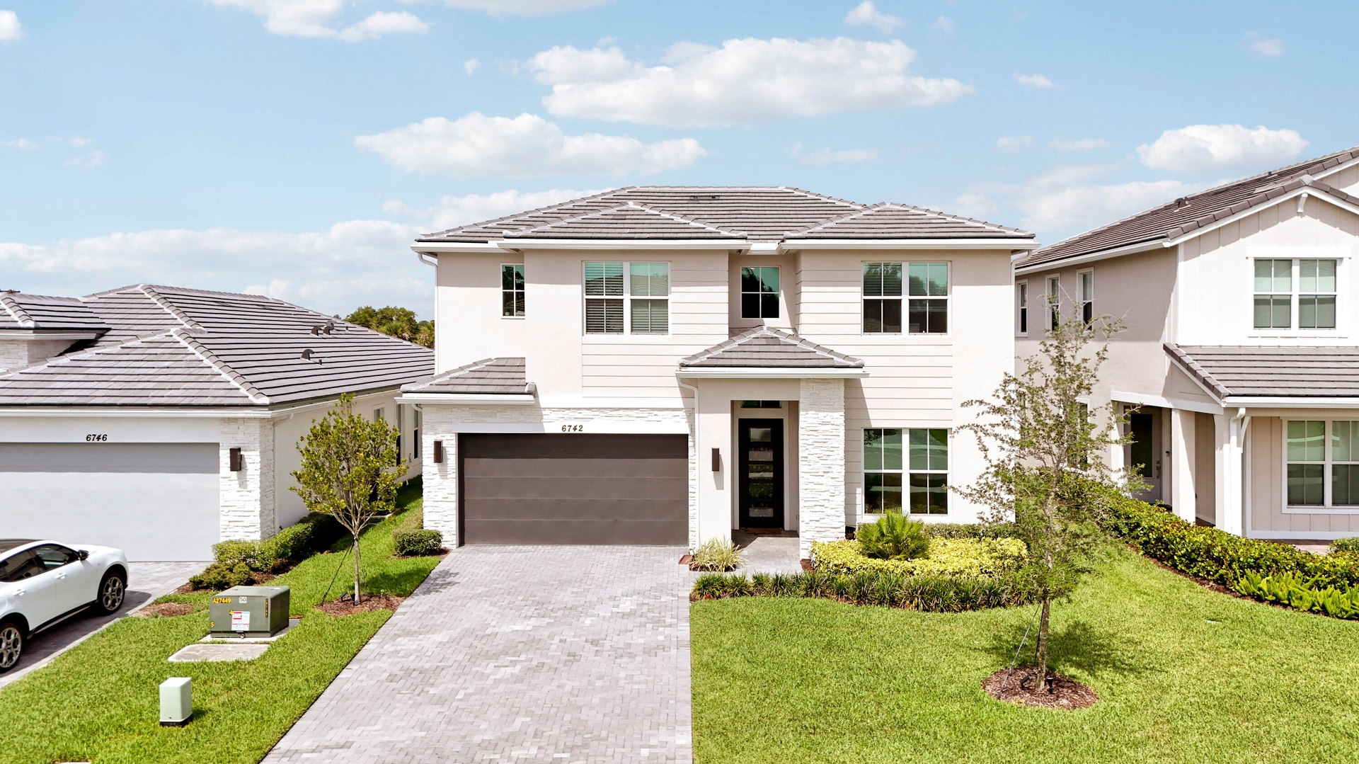 Two-story exterior featuring stone veneer accents, horizontal siding, a tiled roof, and a paved driveway leading to a multi-car garage