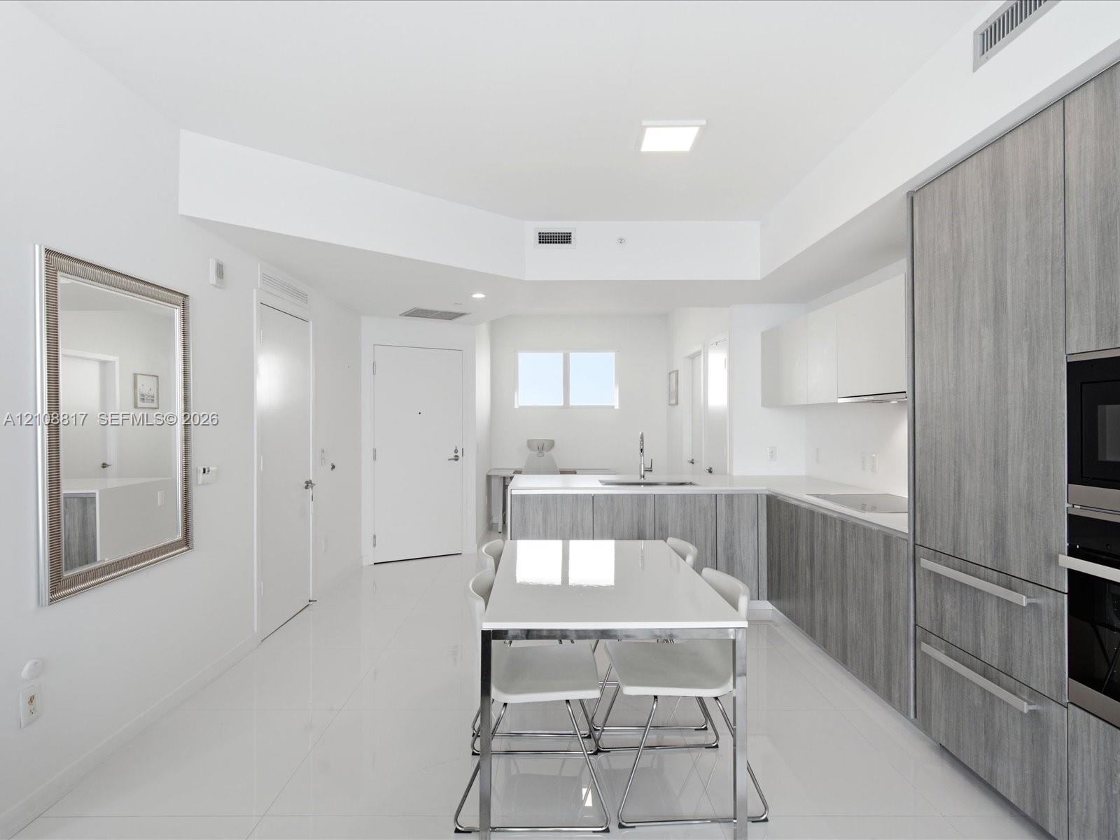 Modern kitchen featuring textured grey cabinetry, white solid-surface countertops, polished white flooring, and built-in stainless steel appliances