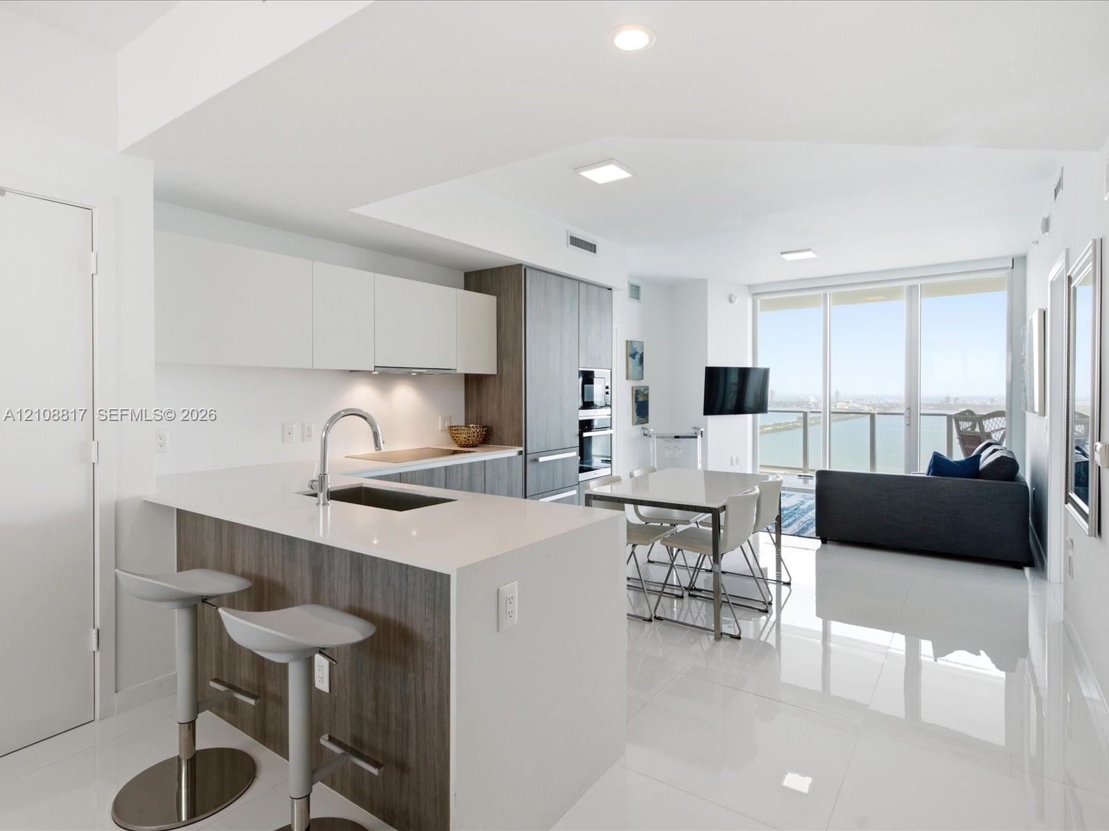 Kitchen featuring two-tone cabinetry, composite countertops, integrated stainless steel appliances, and large-format tile flooring, complete with floo