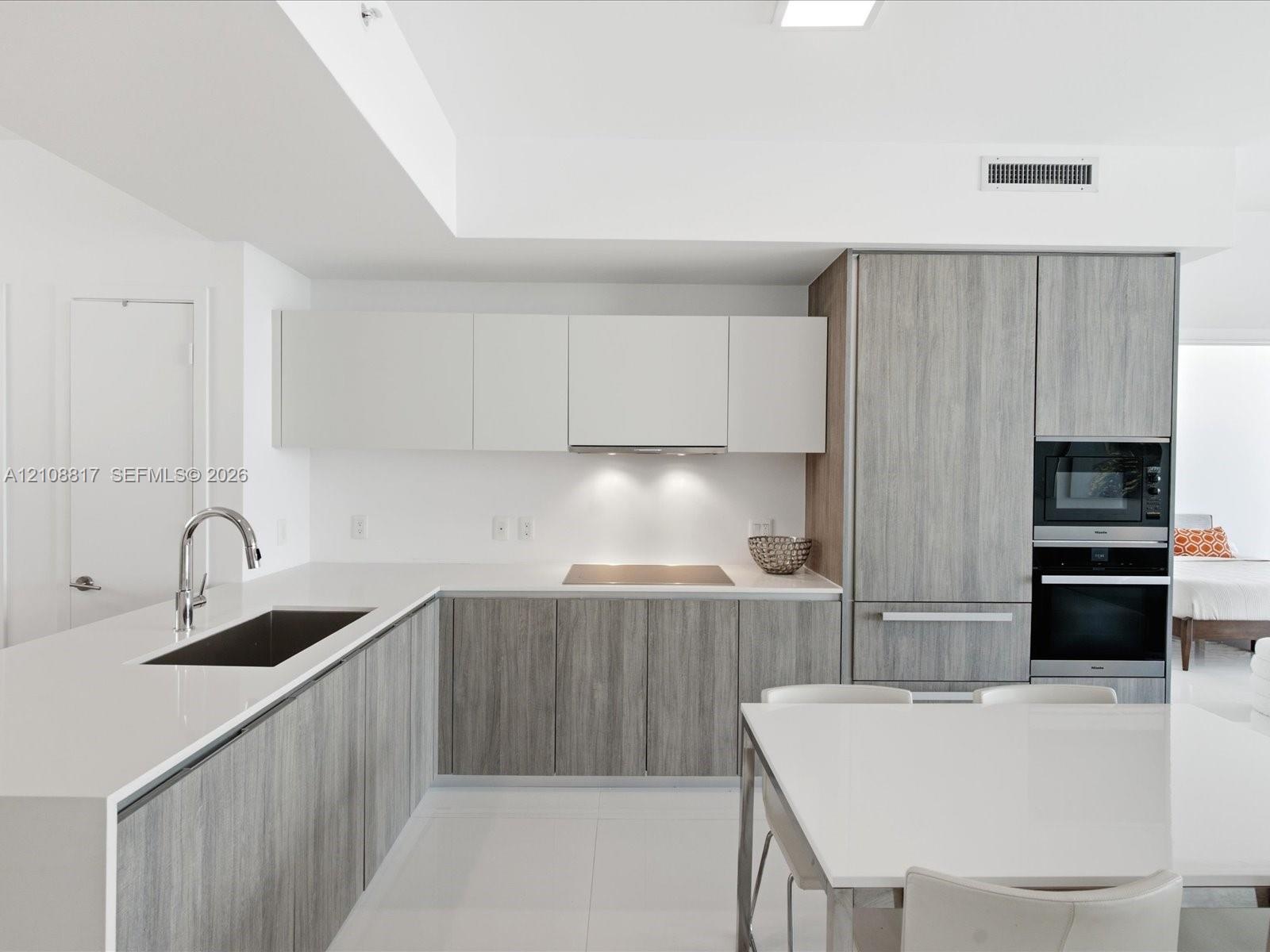 Contemporary kitchen featuring dual-tone cabinetry, quartz countertops, integrated stainless steel appliances, and a recessed stainless steel sink wit
