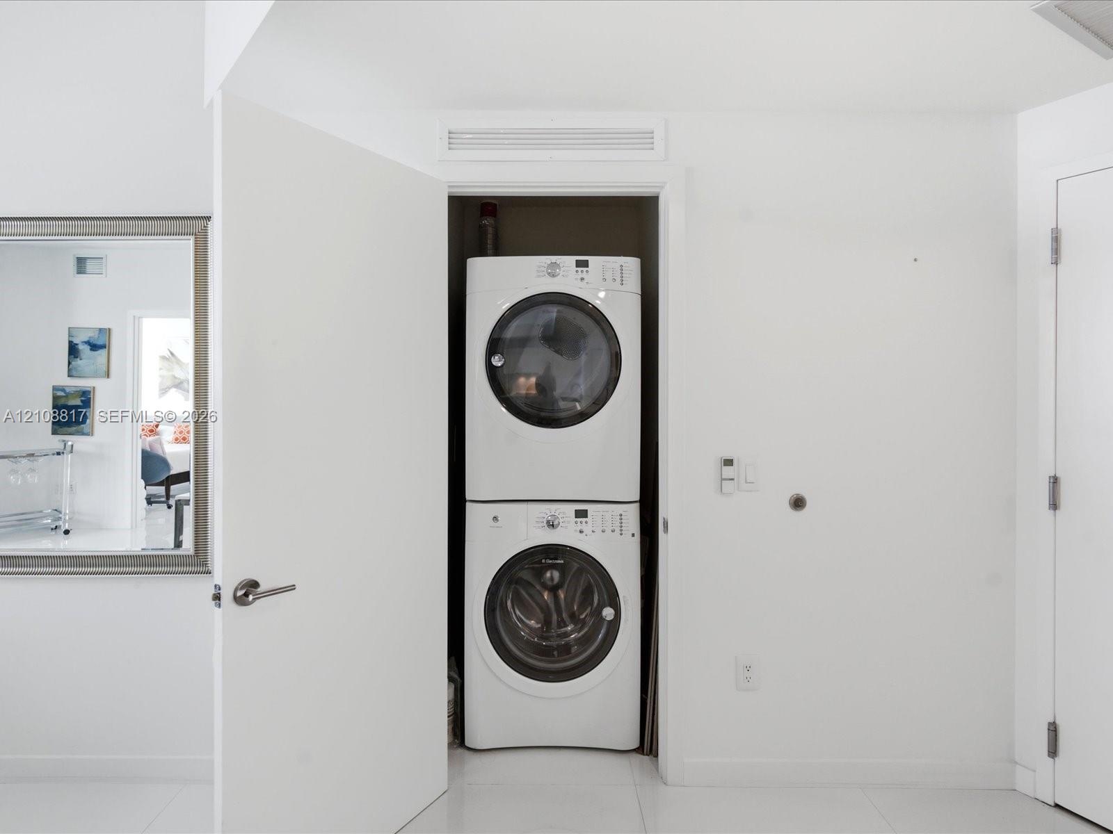 Stackable white front-load washer and dryer unit housed in a recessed closet