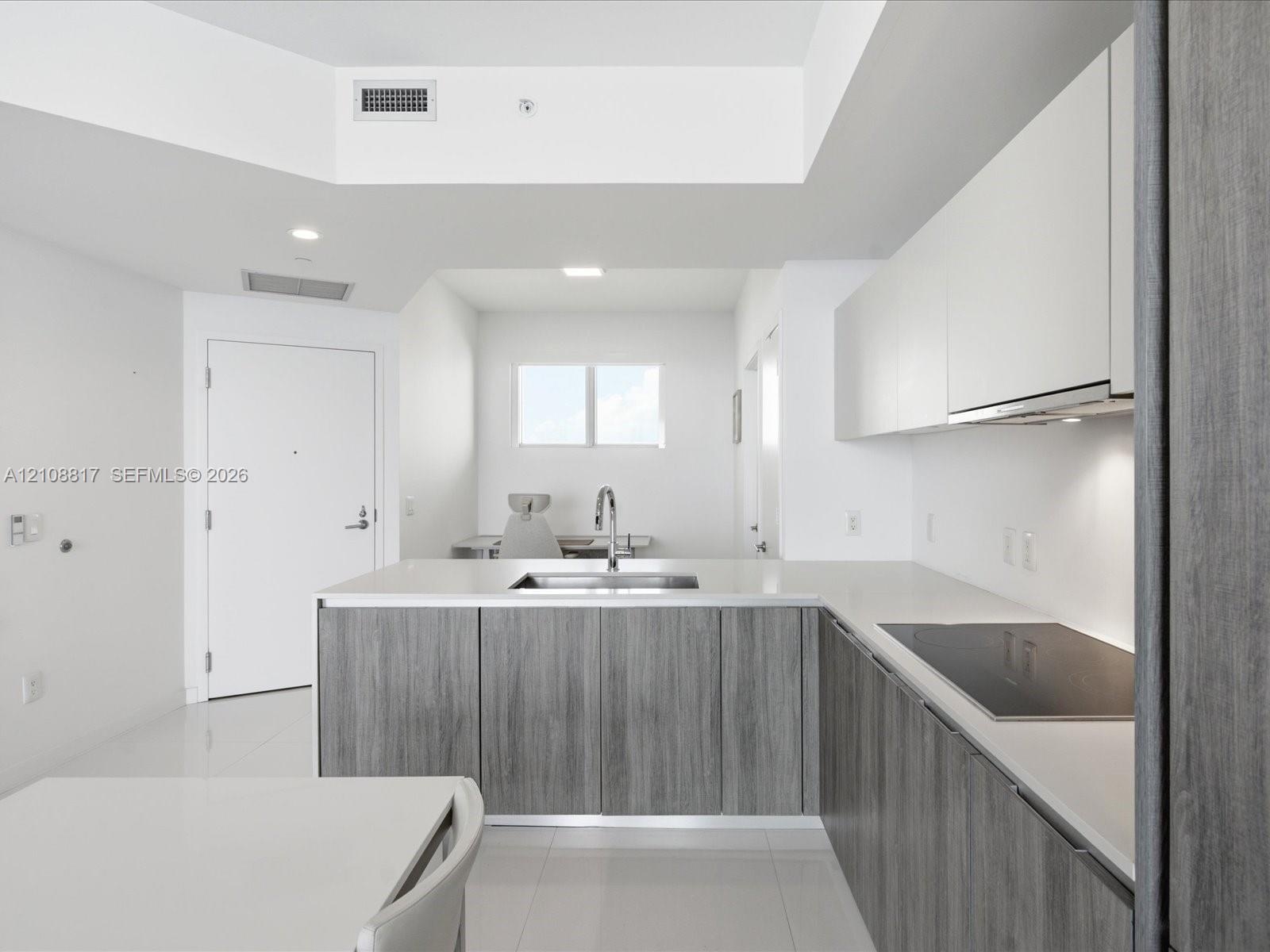 Modern kitchen featuring flat-panel cabinetry with wood-finish lower cupboards, solid surface countertops, an undermount sink with a gooseneck faucet,