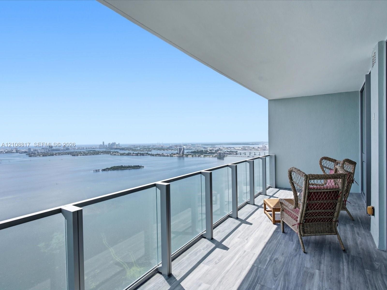 Covered balcony featuring wood-finish flooring and glass-paneled railing with metal framing, overlooking a wide expanse of water