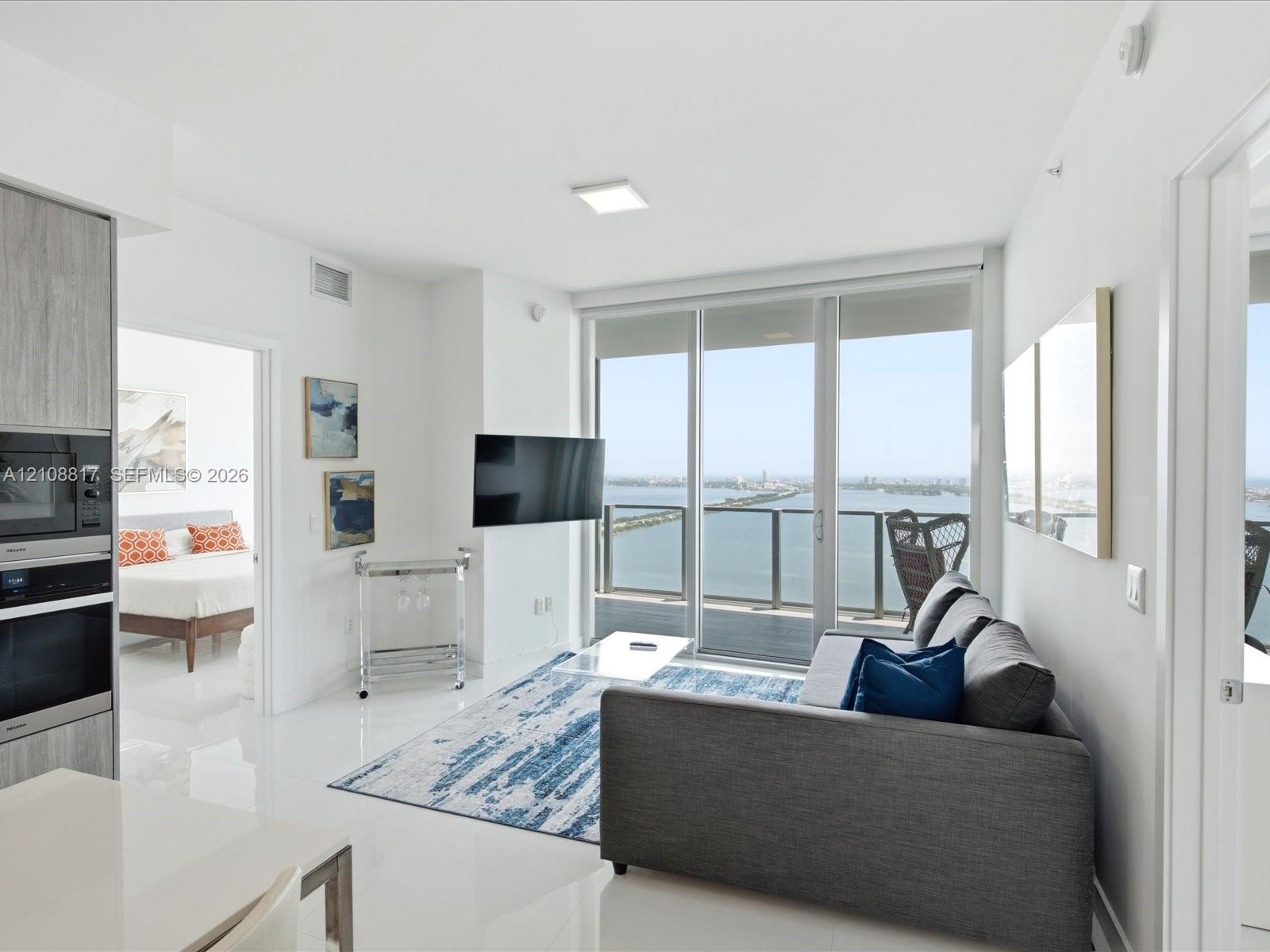 Floor-to-ceiling glass doors, private balcony with water scenery, built-in stainless steel double oven, and polished white tile flooring