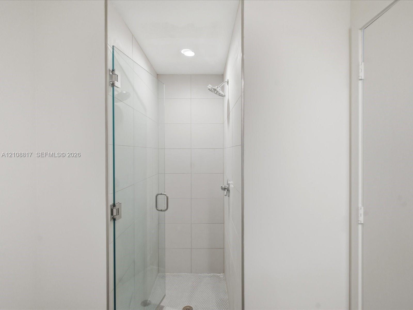 Walk-in shower featuring a frameless glass door, floor-to-ceiling white tile surround, mosaic tile flooring, and a chrome showerhead