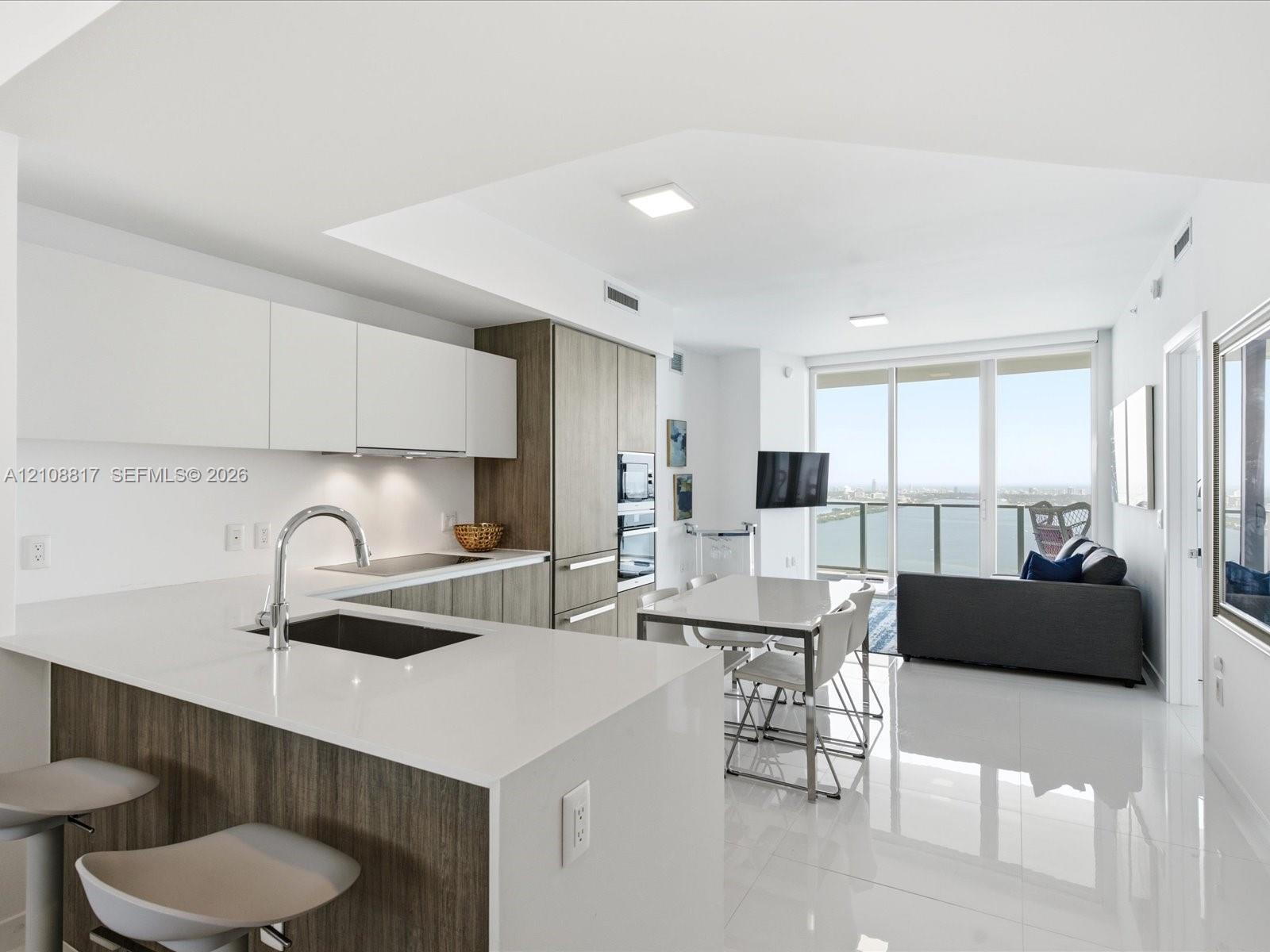 Kitchen featuring matte white cabinetry, wood-finish lower cabinetry, quartz countertops, integrated stainless steel appliances, and large-format tile