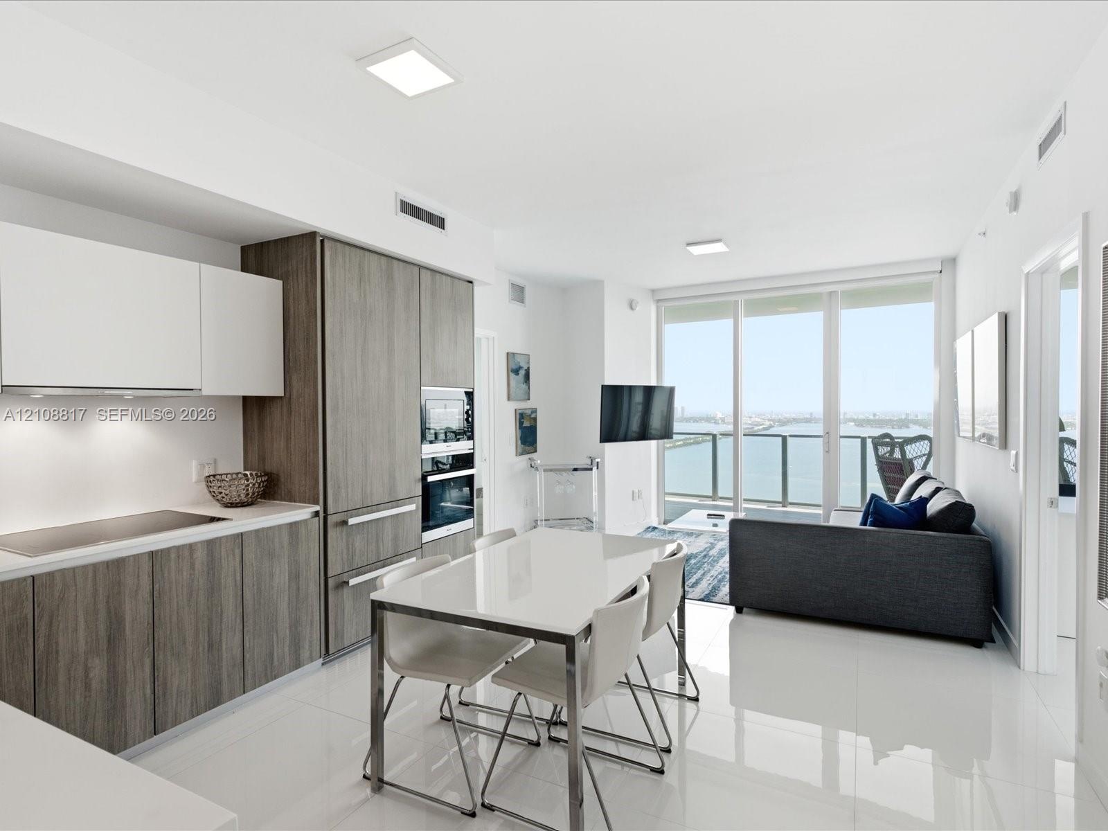 Kitchen featuring two-tone cabinetry with wood-finish and flat-panel white uppers, integrated appliances, white stone countertops, and polished tile f