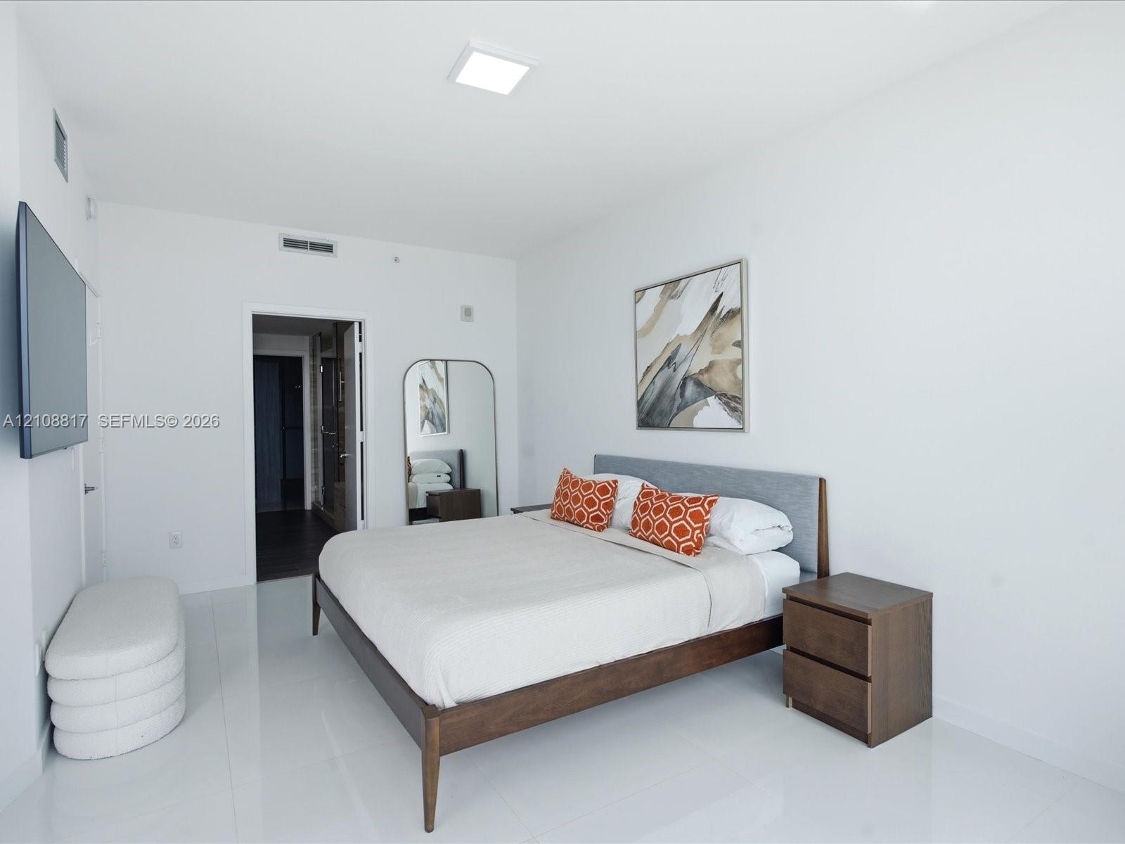 Spacious room featuring high-gloss tile flooring, smooth white walls, recessed ceiling lighting, and a wall-mounted television