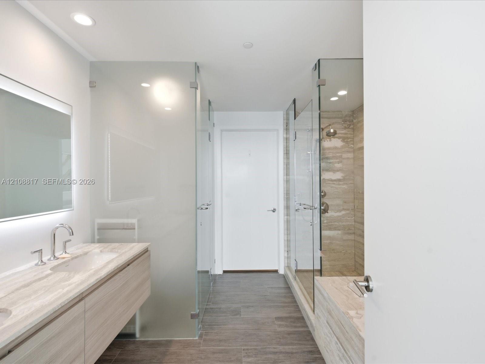 Floating vanity featuring a stone countertop and integrated sink, frameless glass shower enclosure with stone-tile surround, and wood-finish tile floo